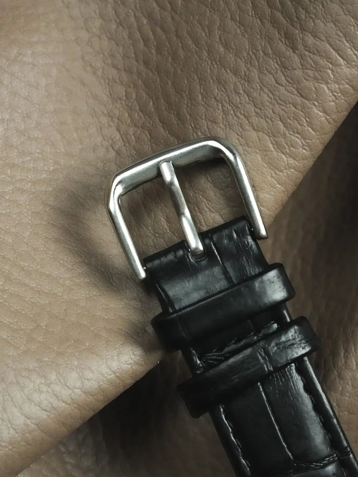 Black alligator leather watch strap with polished steel buckle on textured surface