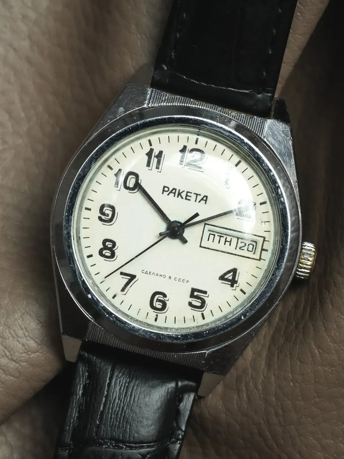 Vintage Raketa watch with white dial, black leather strap, day-date window, worn on wrist