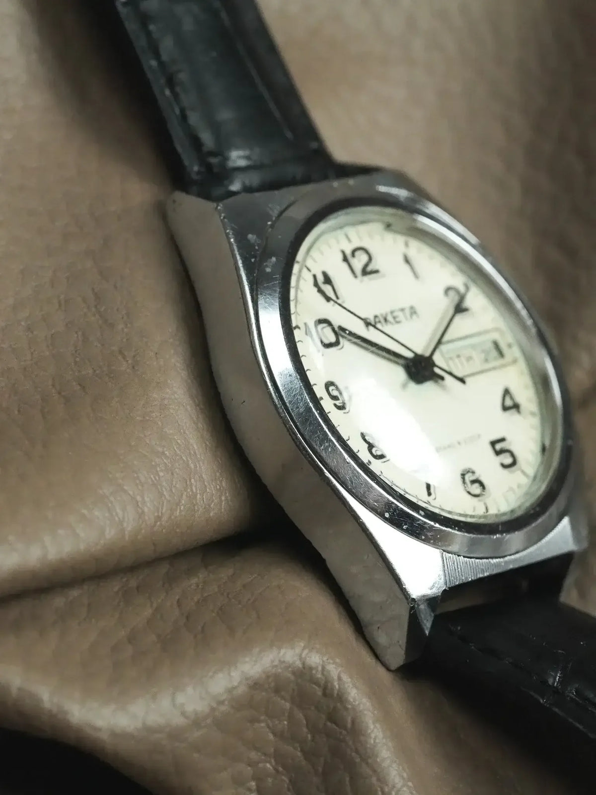 Raketa vintage watch with cream dial, black leather strap, on textured surface