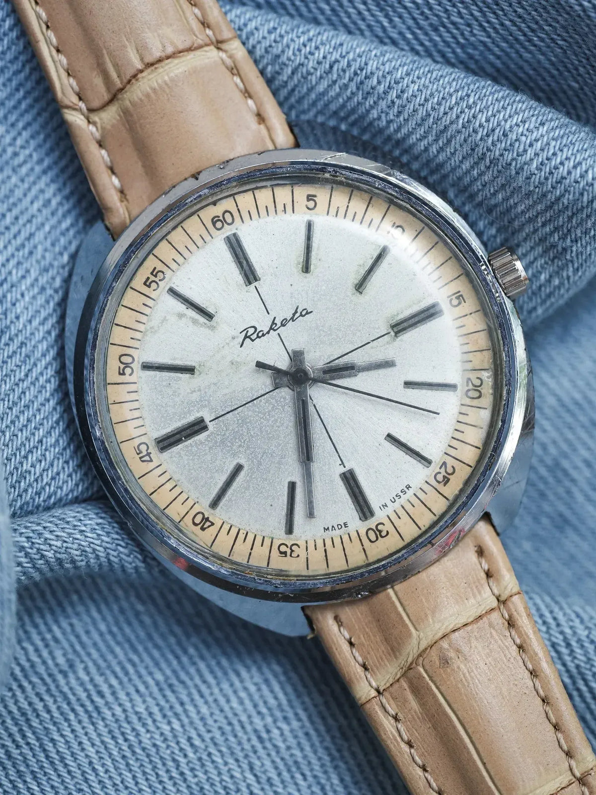 Raketa vintage watch with cream dial, steel case, and tan leather strap on denim