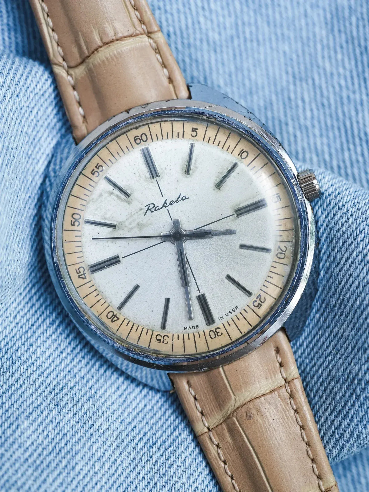 Raketa vintage watch with cream dial, steel case, tan leather strap on denim
