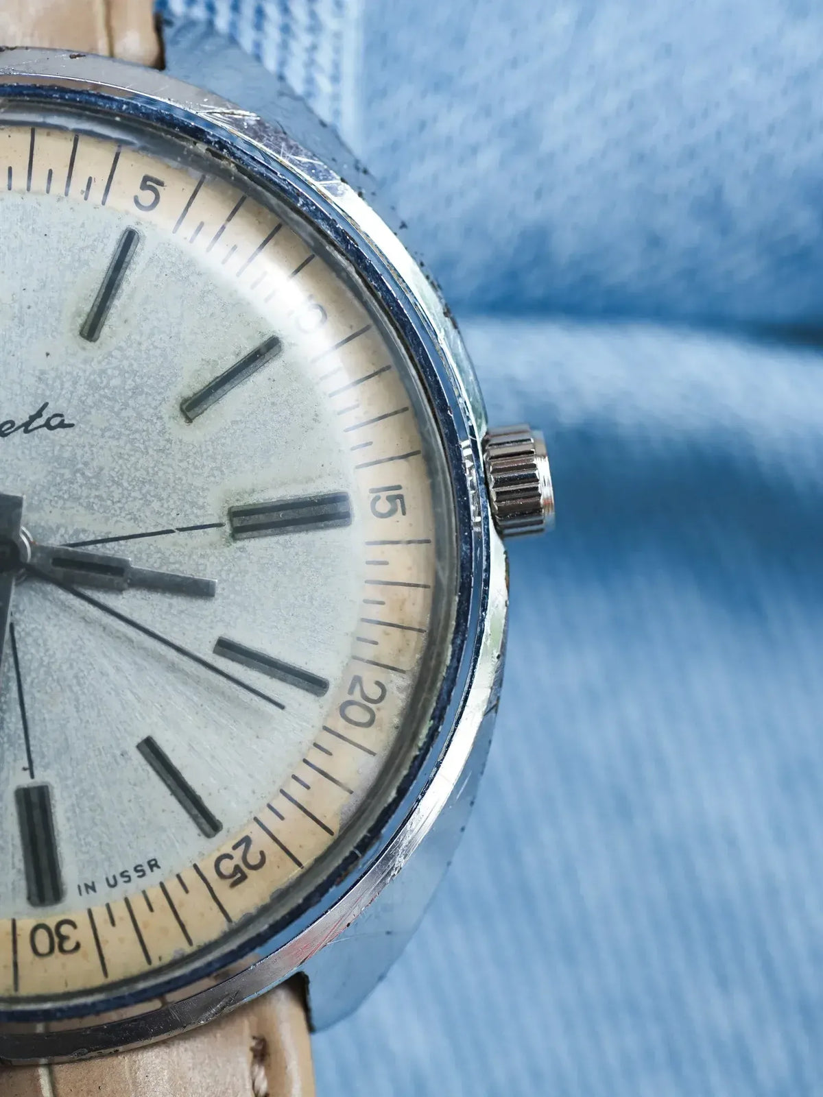 Vintage Vostok watch with silver dial, cream bezel, and leather strap on blue fabric