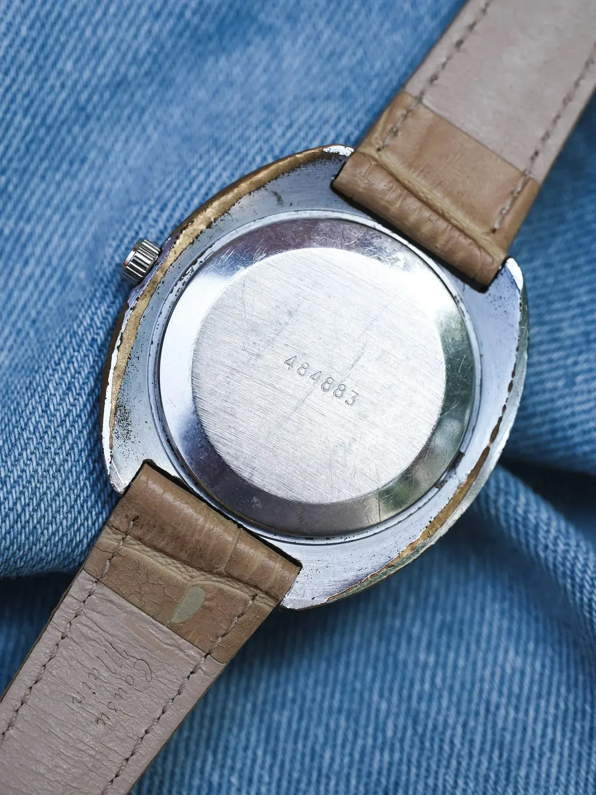 Vintage watch with stainless steel case back and brown leather strap on denim