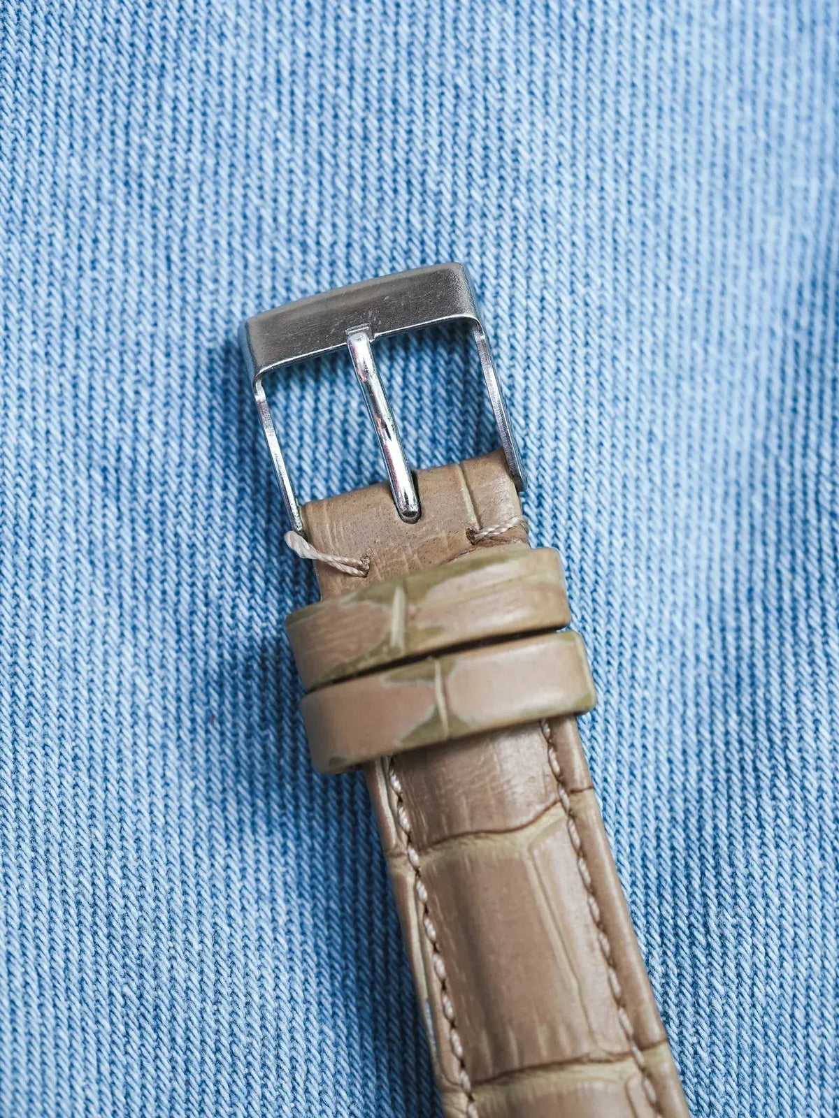 Beige alligator leather watch strap with silver buckle on denim background