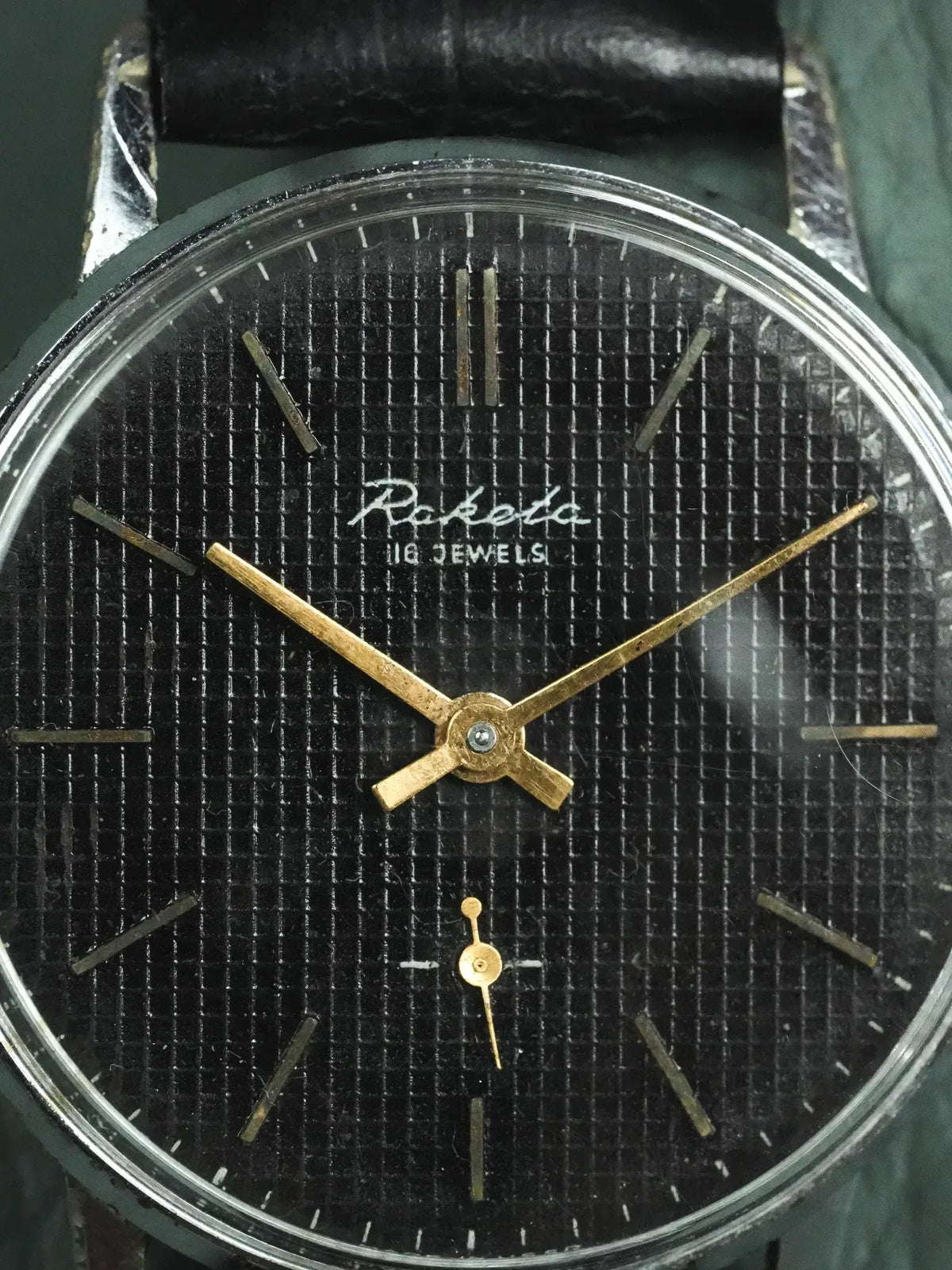 Raketa vintage watch with black textured dial, gold hands, and leather strap