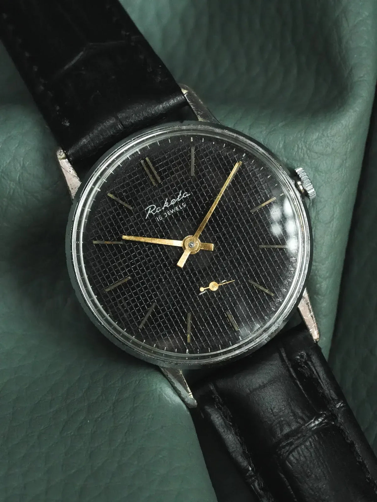 Raketa vintage watch with black textured dial, gold hands, and black leather strap
