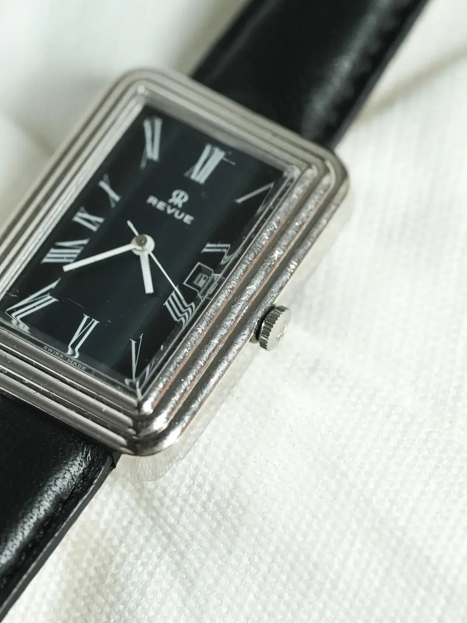 Revue vintage watch with black dial, Roman numerals, and black leather strap on white background