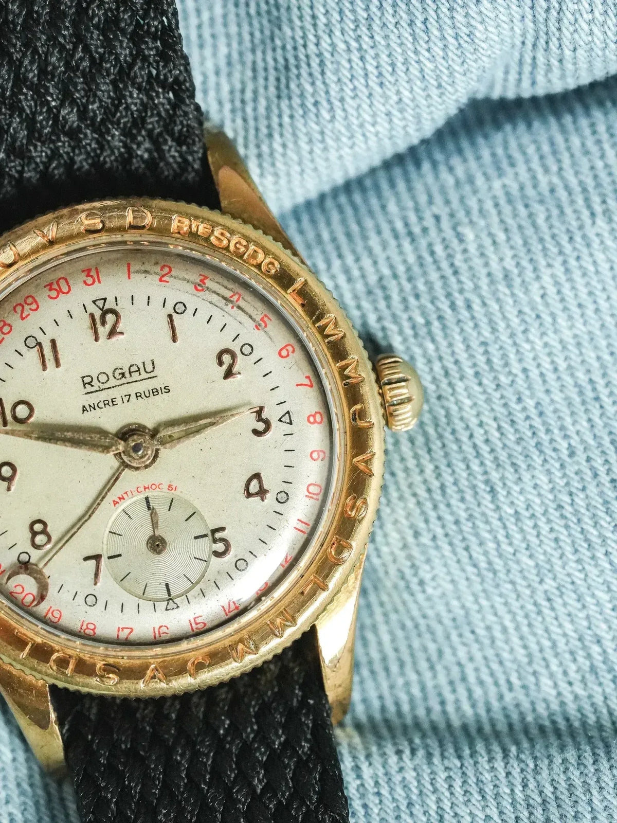Rogau vintage watch with gold case, cream dial, red date, black strap on denim