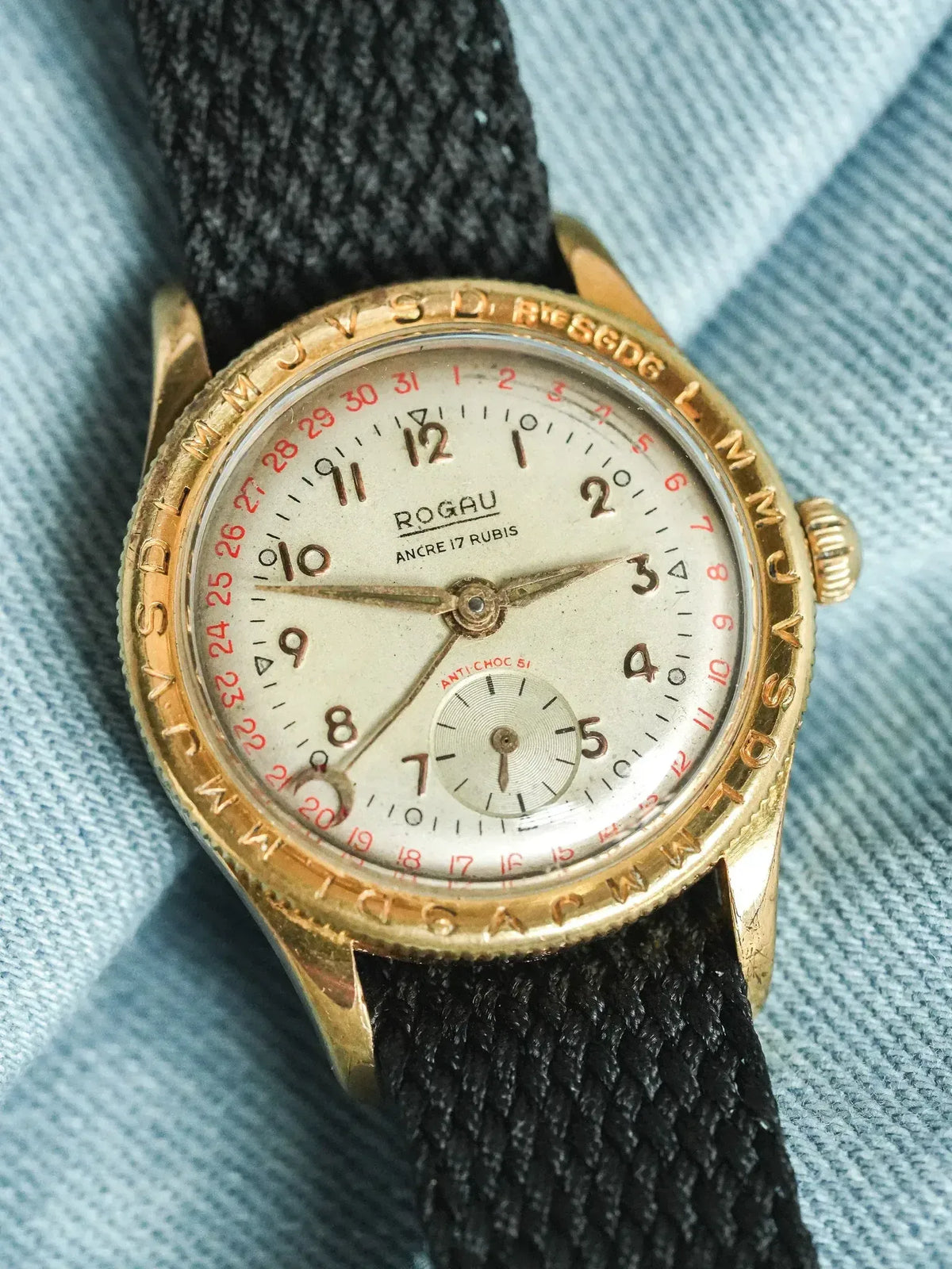 Rogau vintage watch with gold case, cream dial, red date numbers, black fabric strap