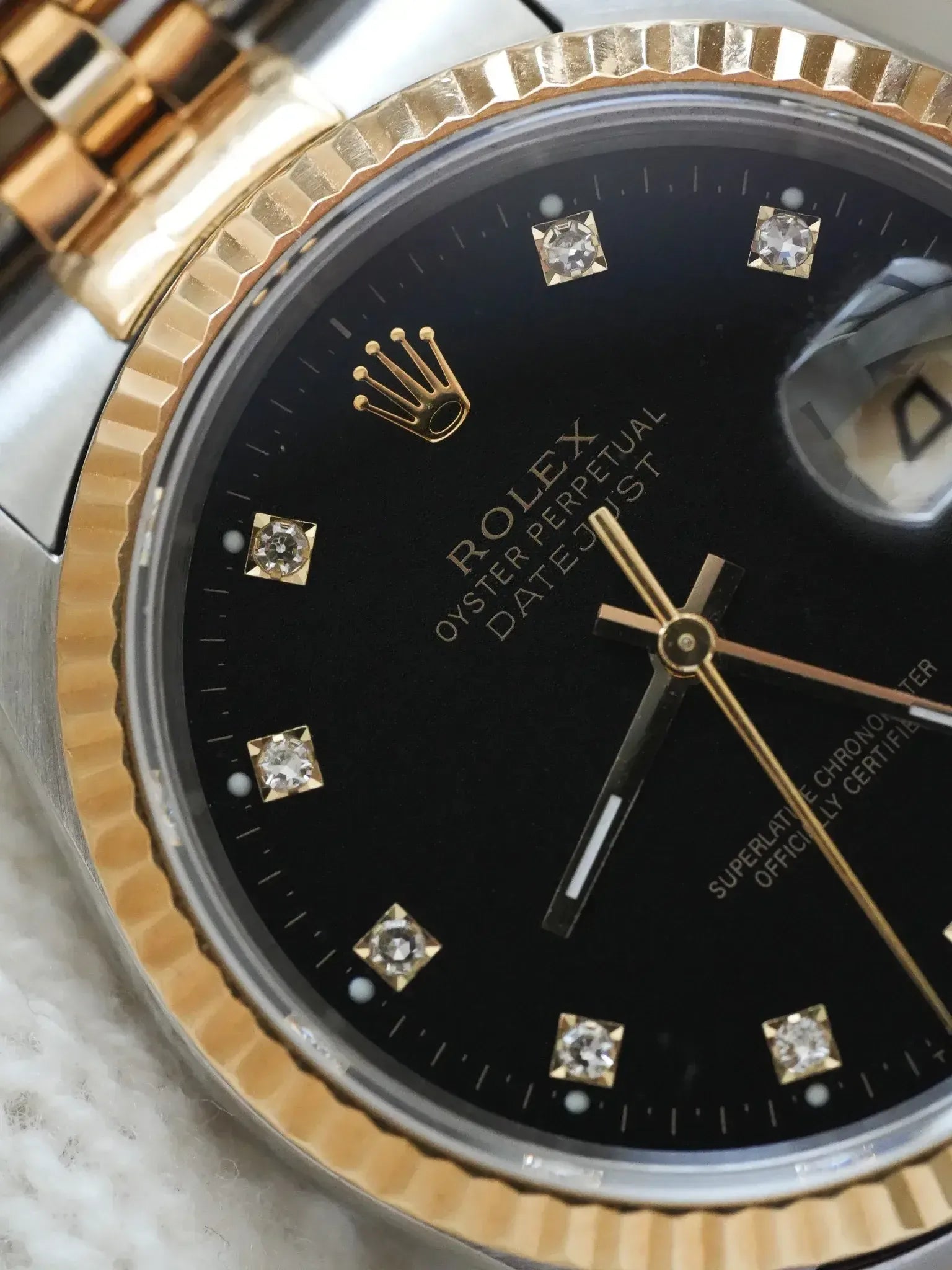 Rolex Oyster Perpetual Datejust with black dial, diamond hour markers, and gold bezel
