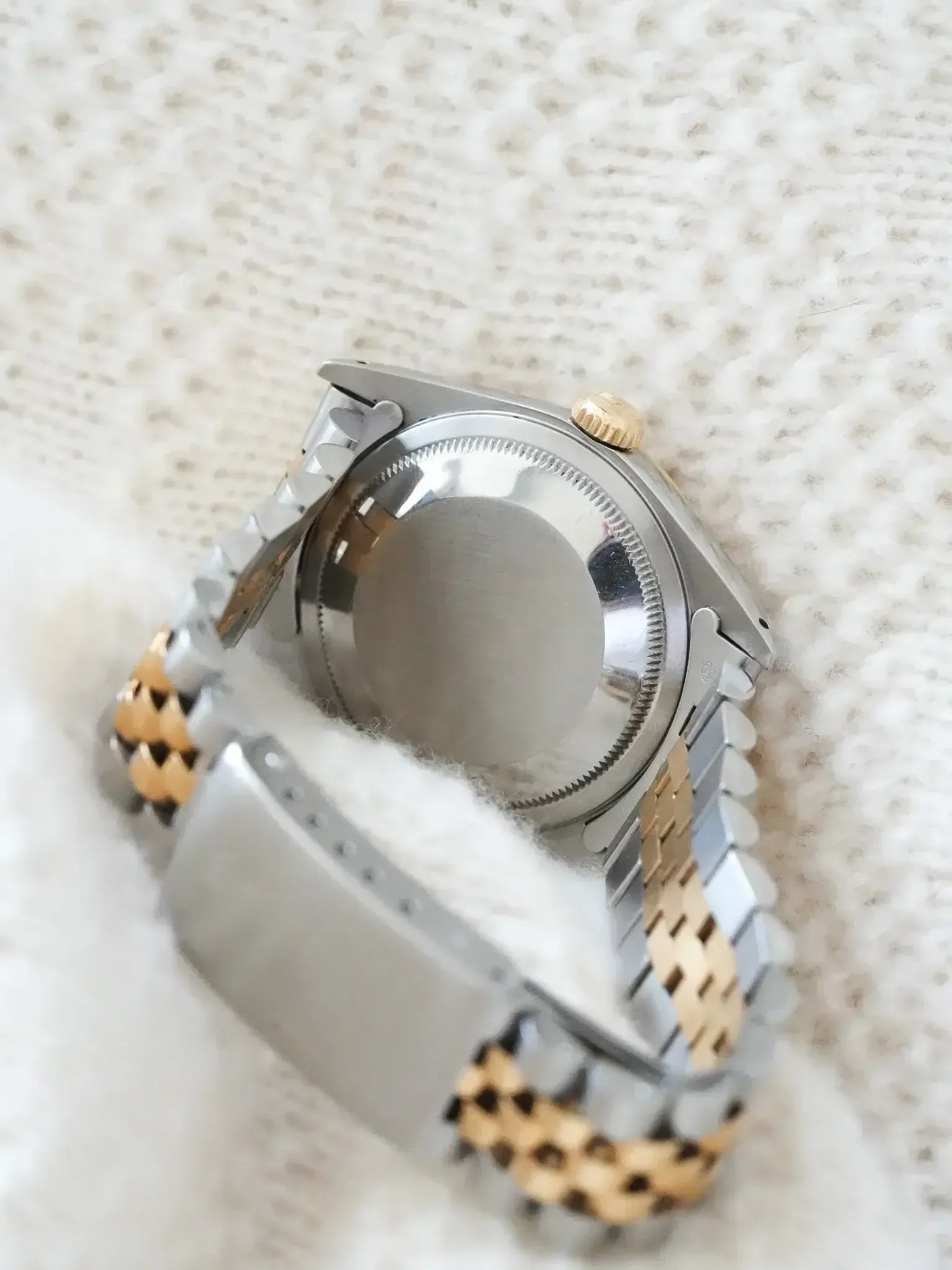 Rolex vintage watch back view, two-tone steel and gold bracelet on textured white fabric