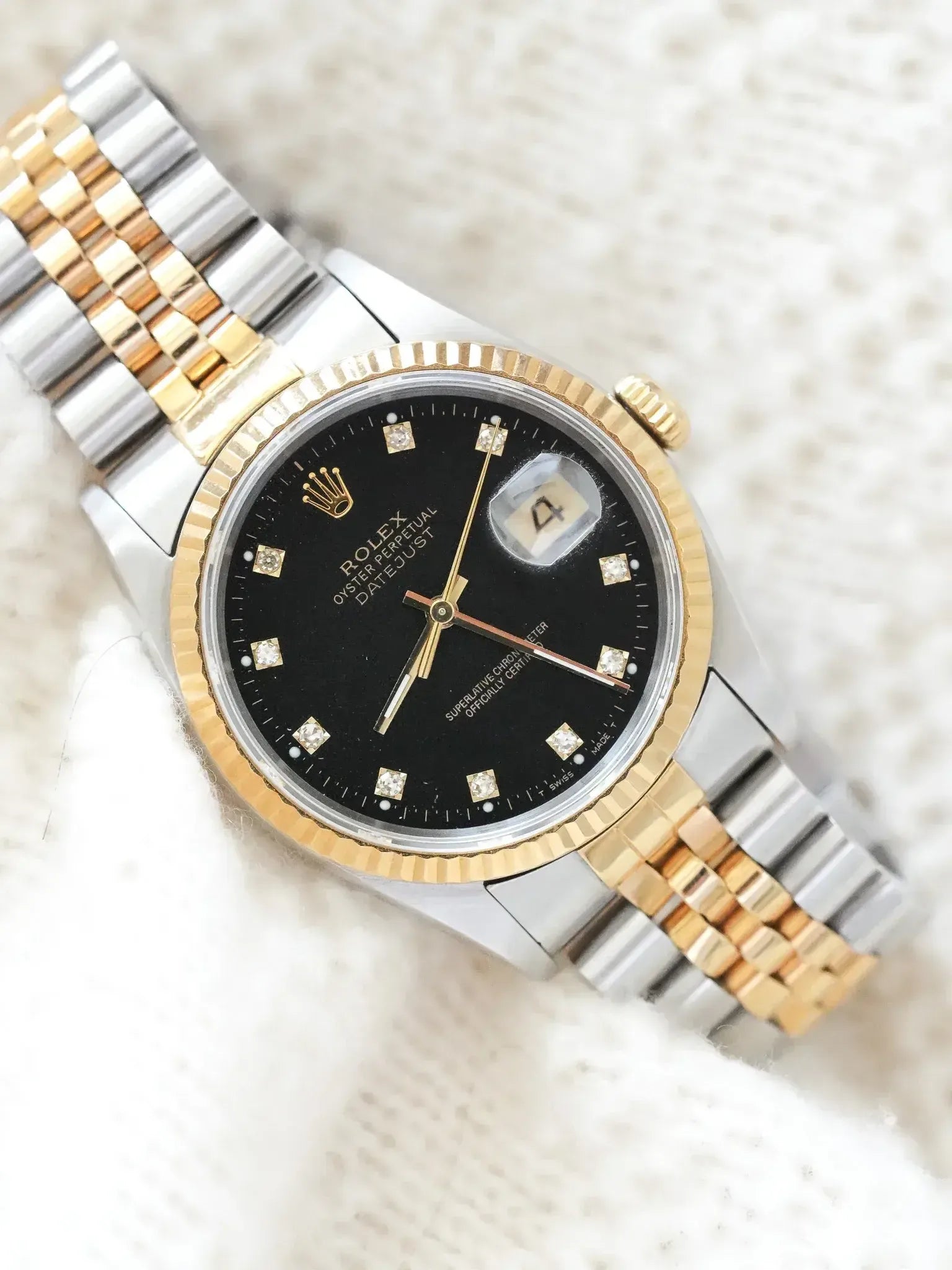 Rolex Datejust vintage with black dial, diamond markers, and two-tone bracelet on textured white background