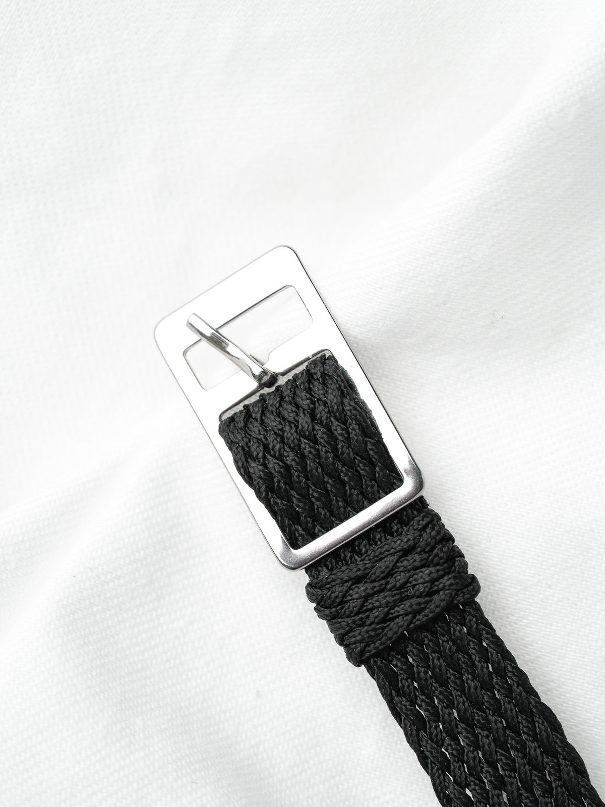 Boucle d'ardillon en acier et bracelet tressé noir sur fond de tissu blanc