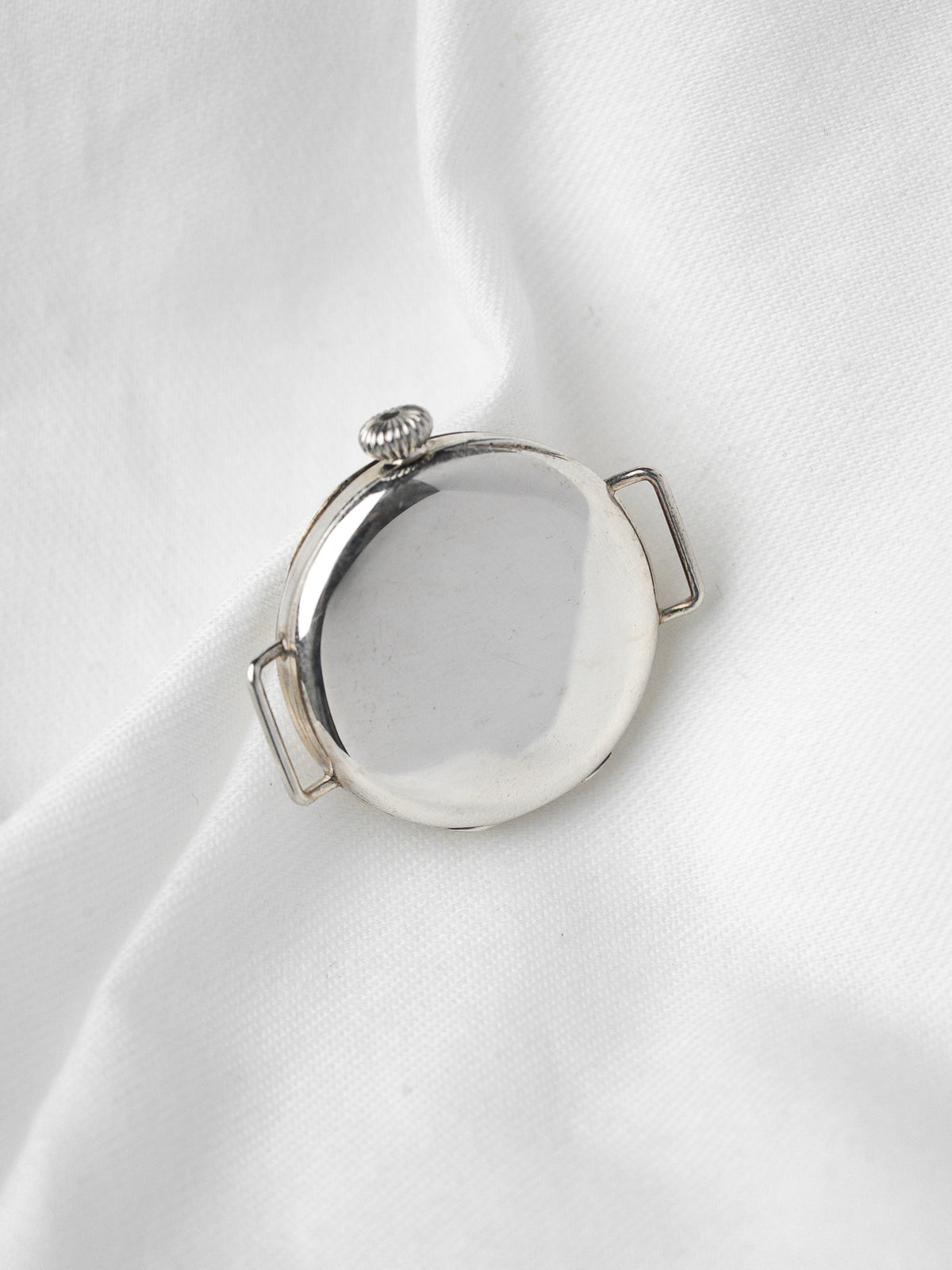 Dos d'une montre vintage en argent avec boîtier rond sur fond tissu blanc