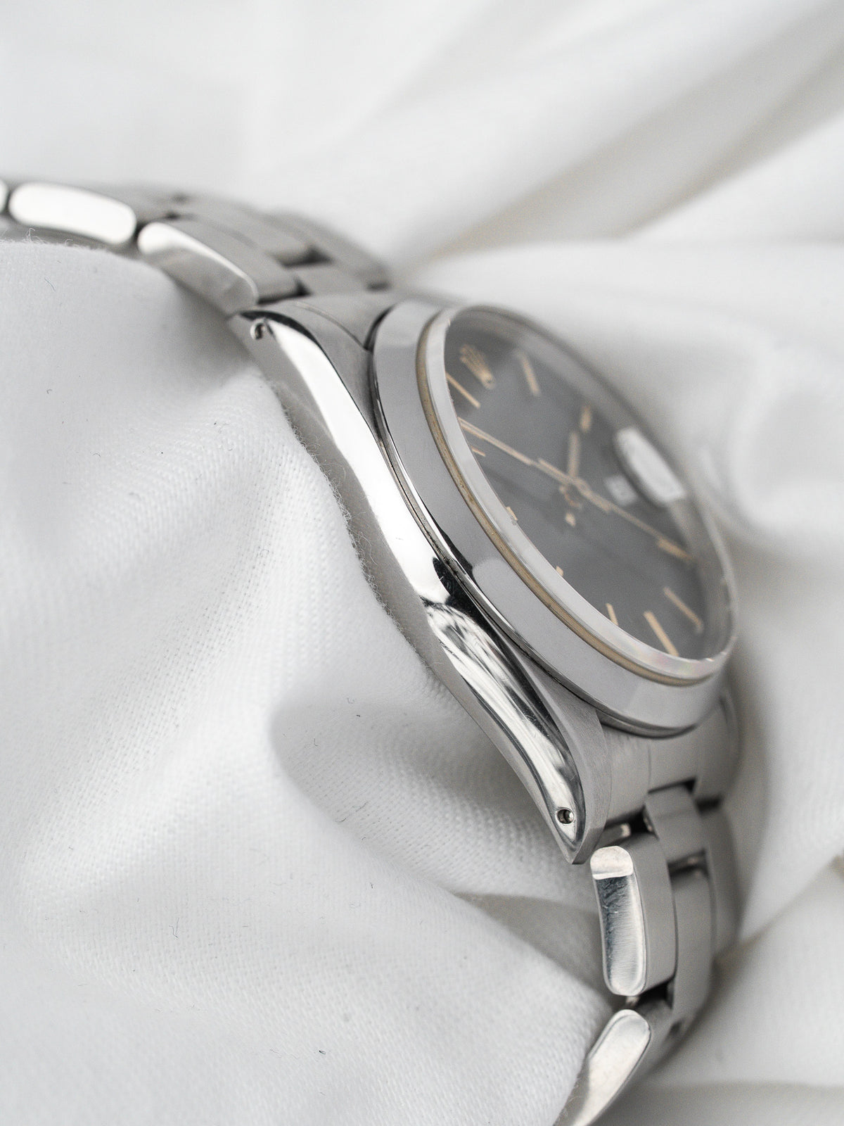 Montre vintage en acier avec cadran noir, posée sur un tissu blanc satiné