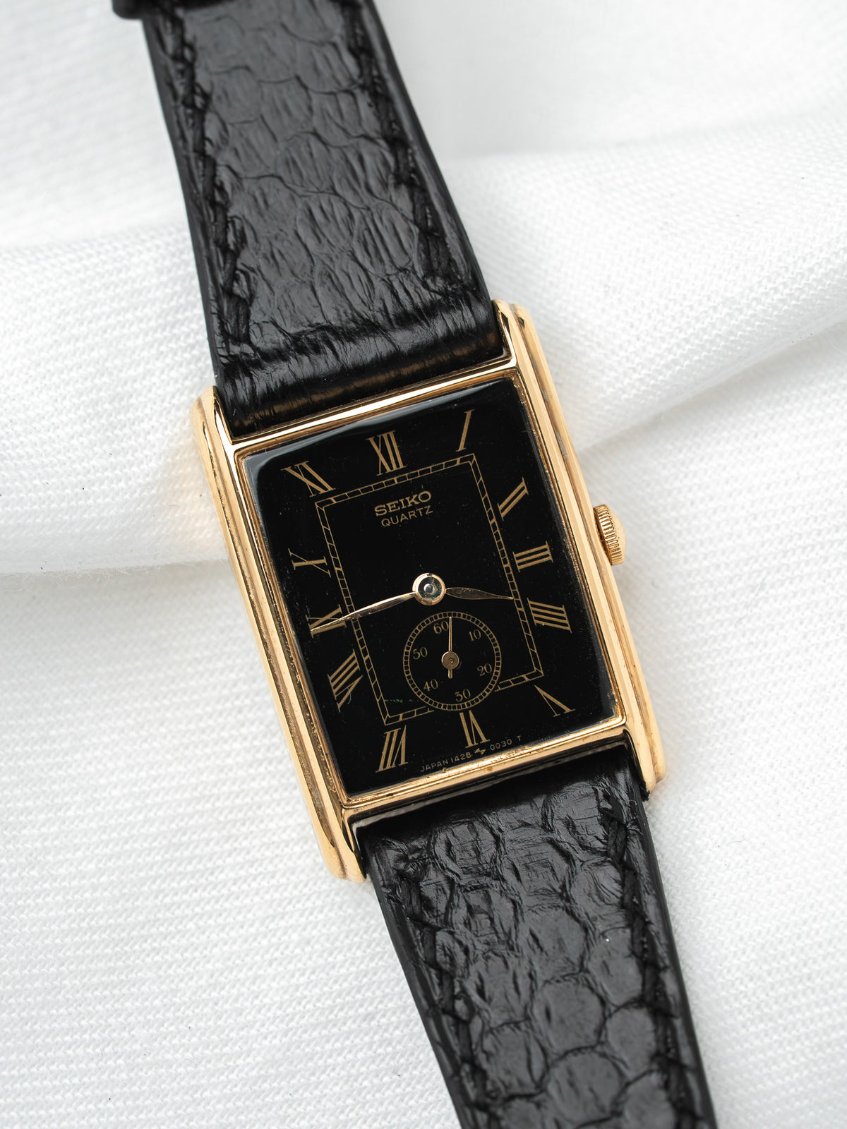 Seiko Quartz vintage watch with gold case, black dial, Roman numerals, and black crocodile strap