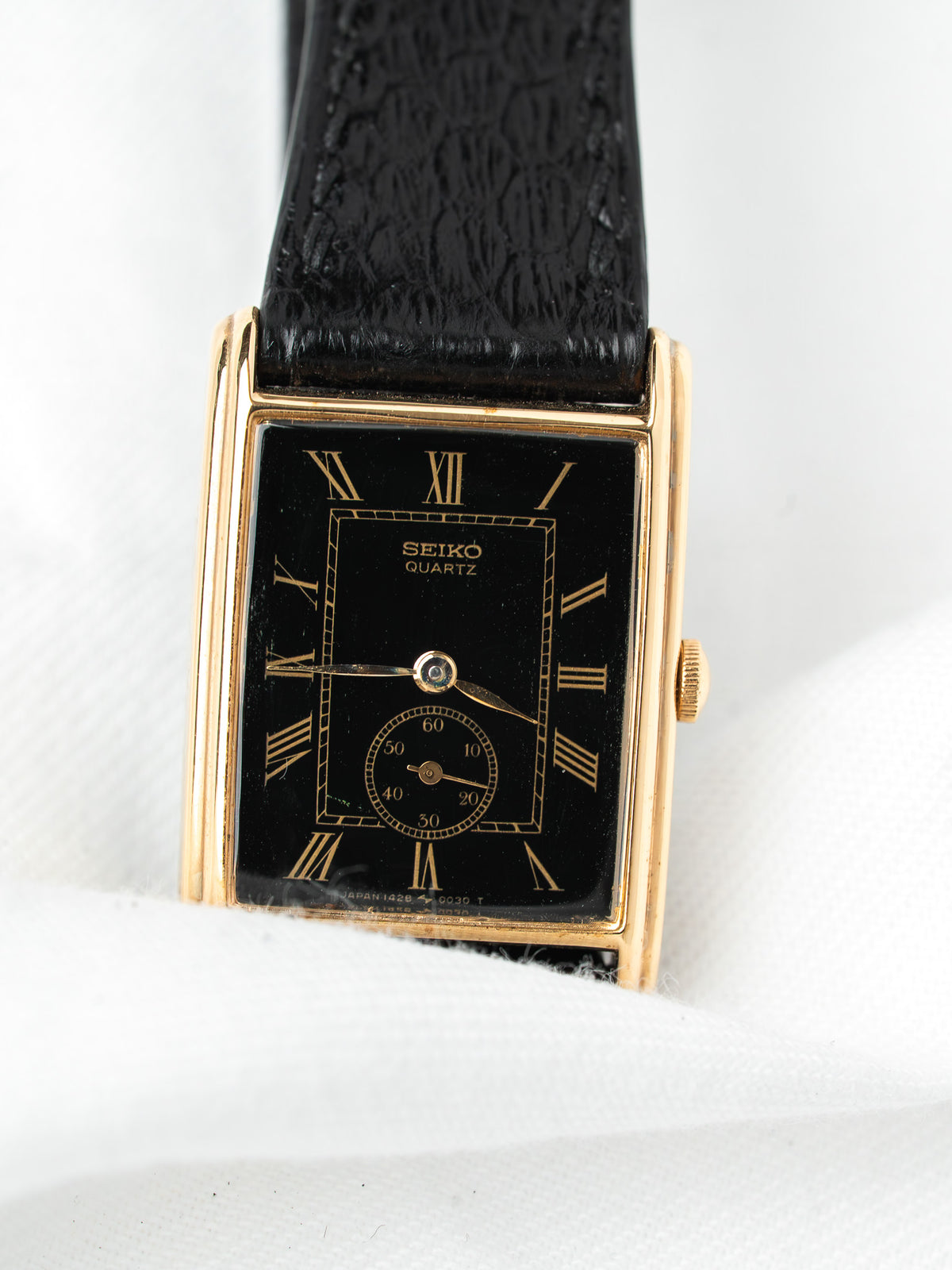 Seiko Quartz vintage watch with gold case, black dial, Roman numerals, and textured strap