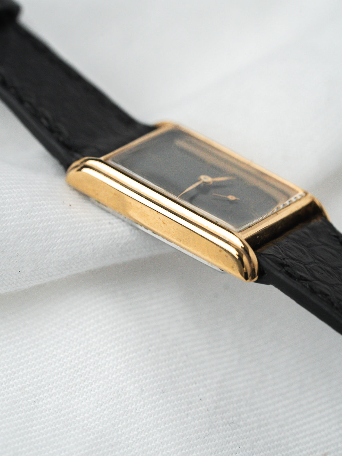 Vintage Cartier Tank watch with gold case, black dial, and black leather strap on white background
