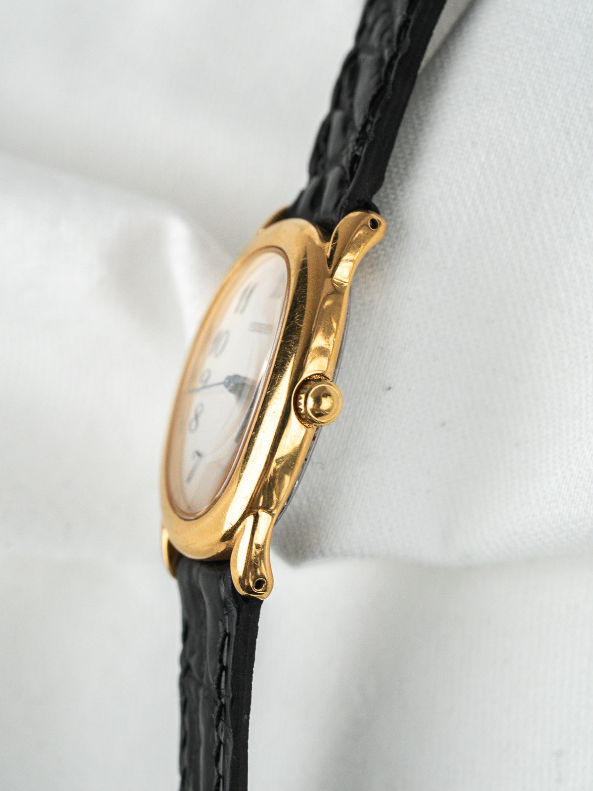 Montre vintage au boîtier or et bracelet en cuir noir sur fond blanc