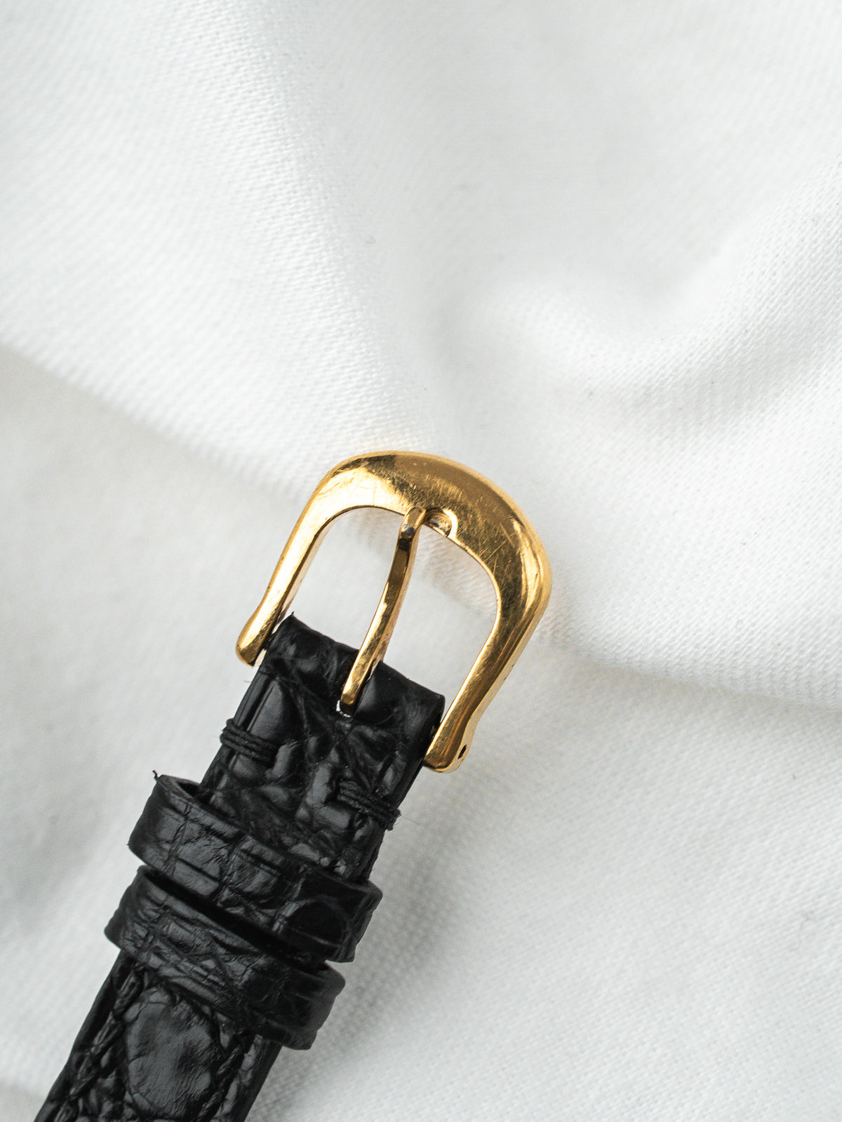 Bracelet de montre en cuir noir façon croco avec boucle dorée sur fond blanc