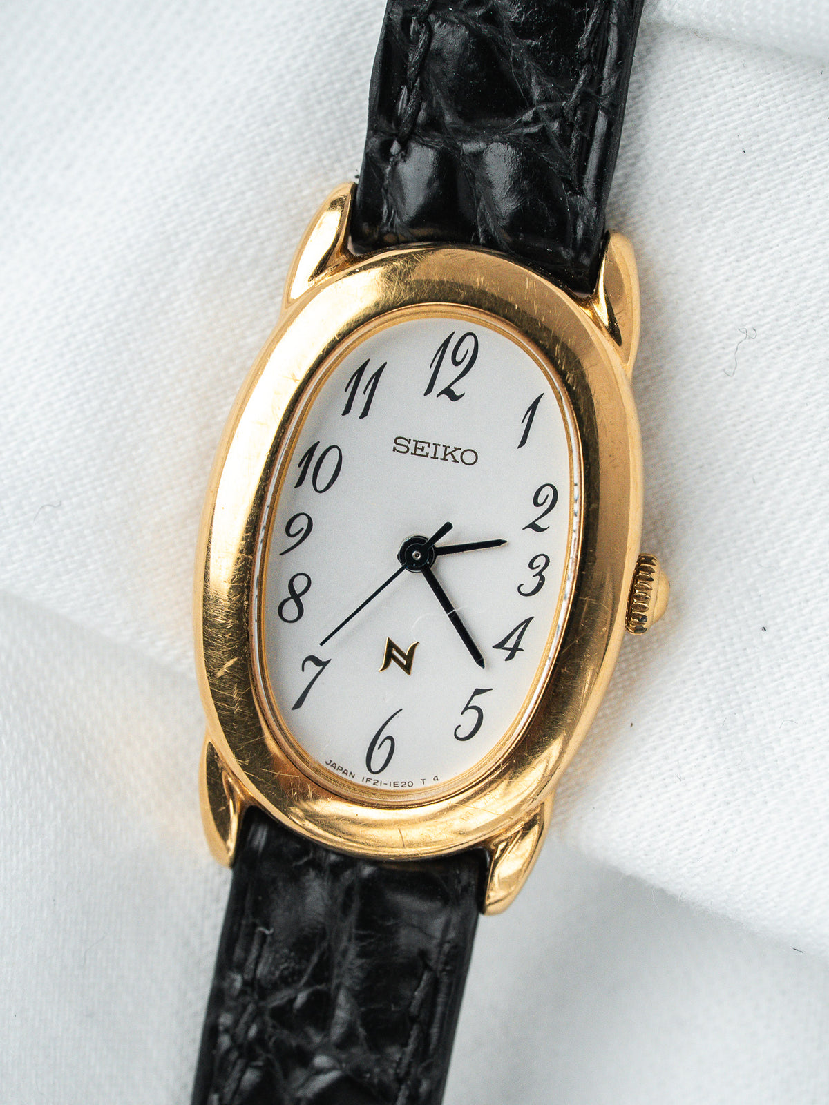 Montre Seiko vintage, boîtier ovale doré, cadran blanc et bracelet en cuir noir