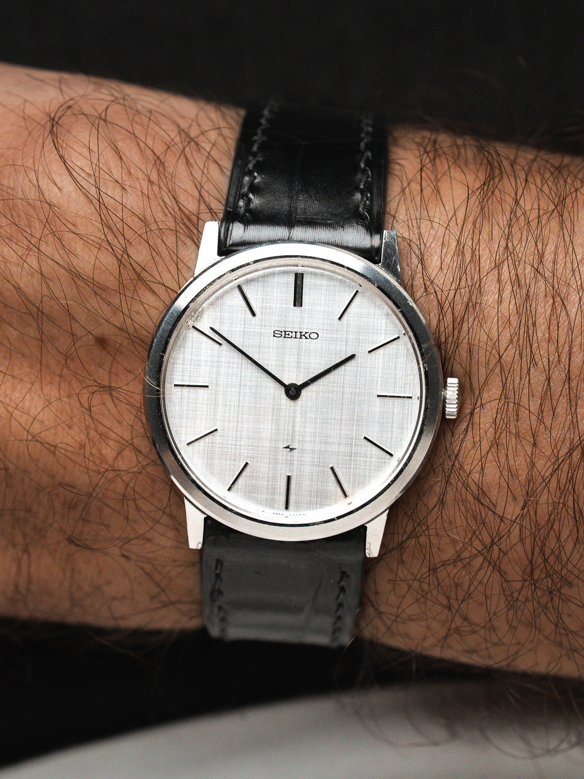 Montre Seiko avec cadran argenté et bracelet en cuir noir portée au poignet.