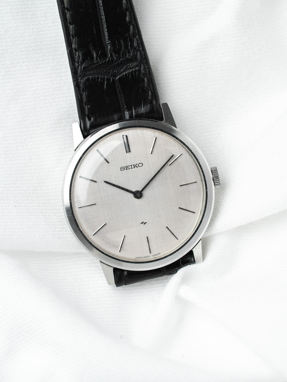 Seiko vintage watch with silver dial, black leather strap on white fabric