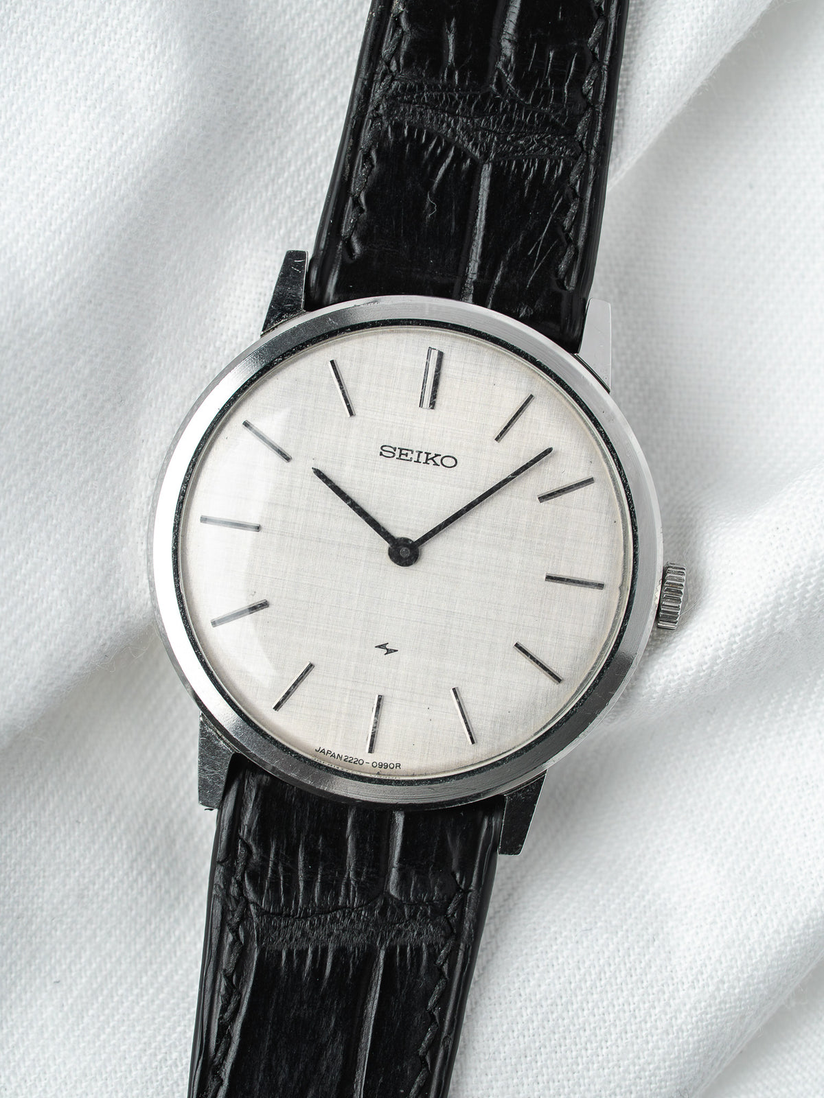 Seiko vintage watch with silver dial, black leather strap, on white fabric background