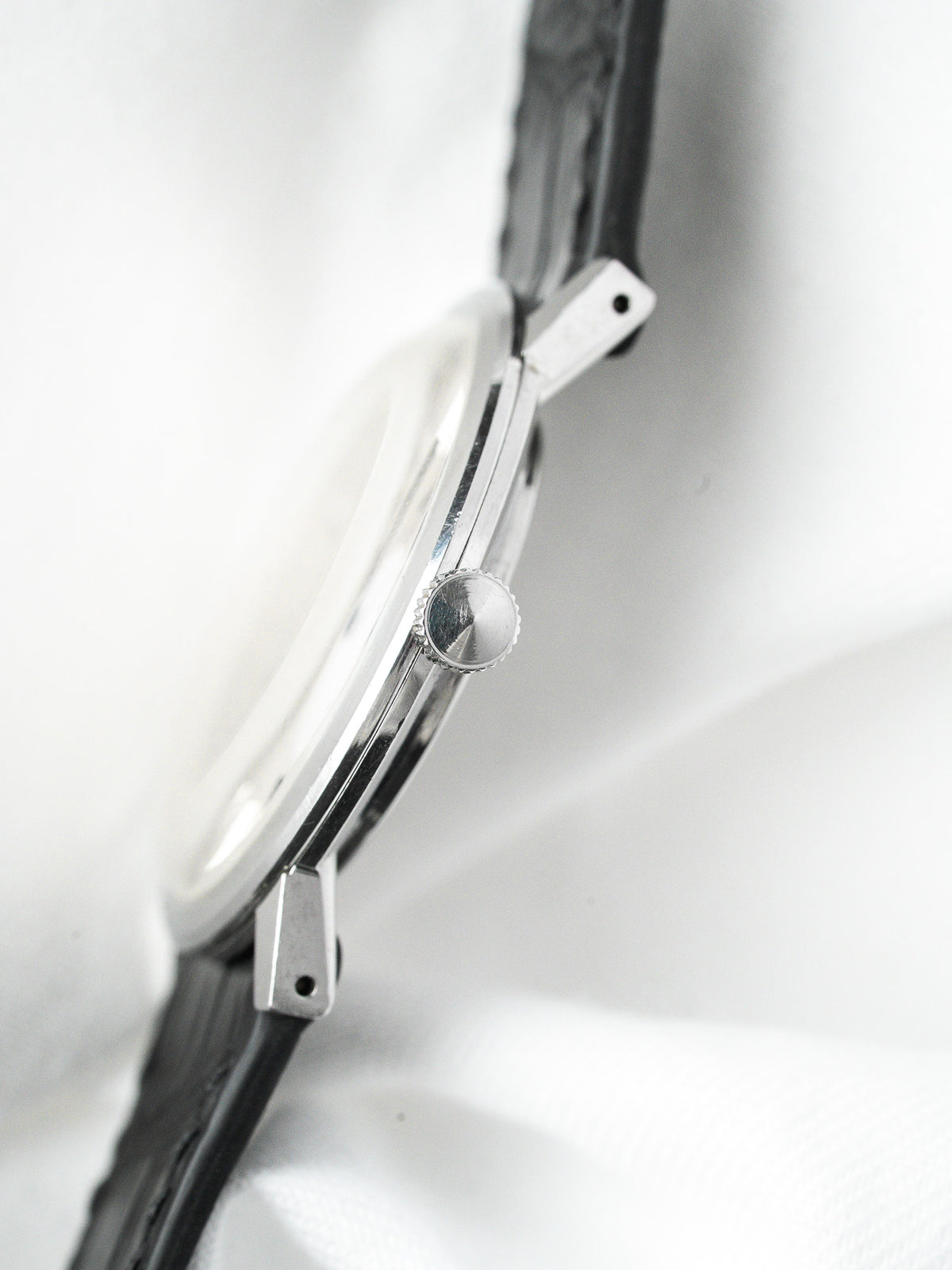 Vintage watch with steel case, black strap, and textured crown on white background