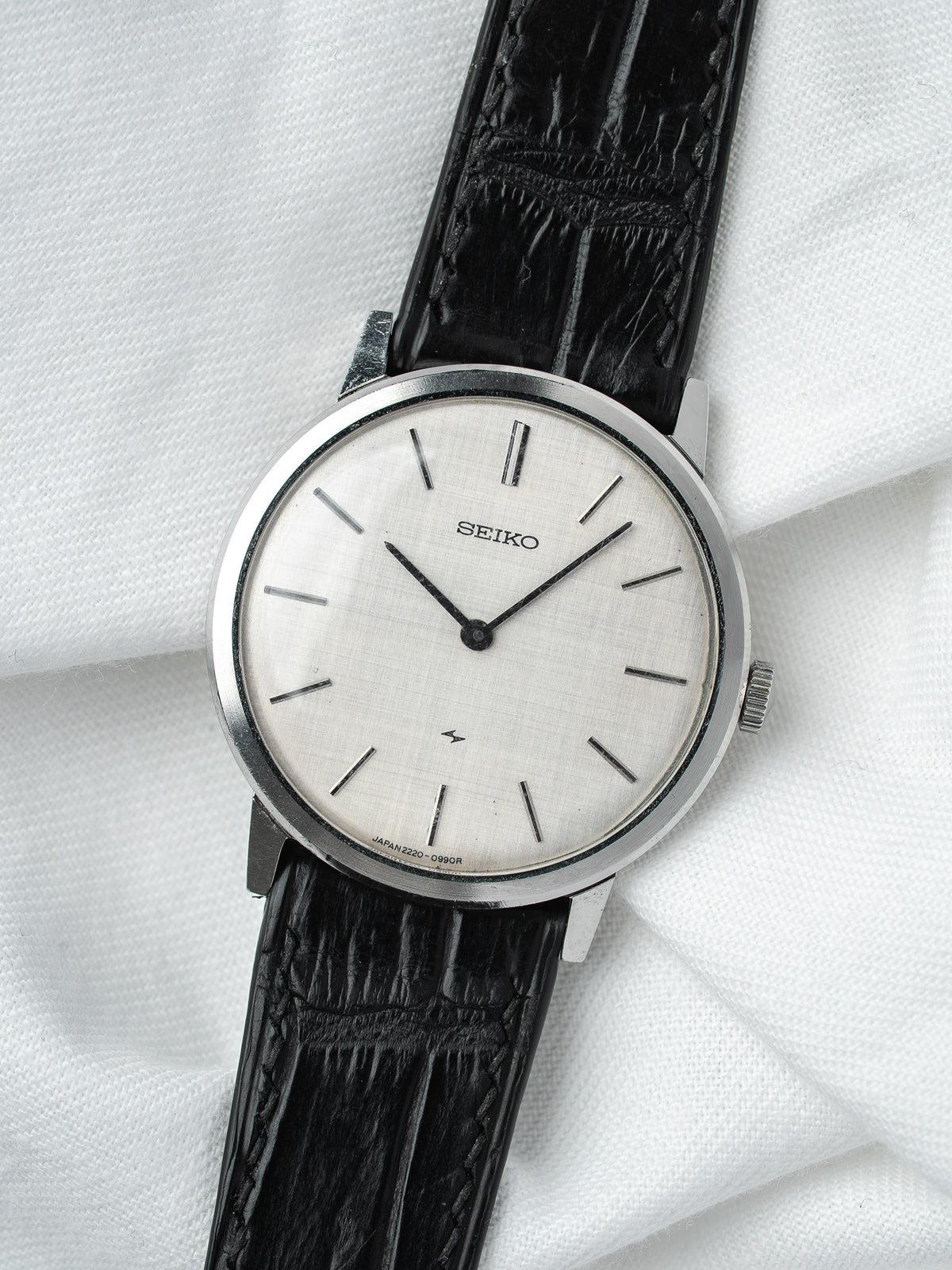 Seiko vintage watch with silver dial, black leather strap, on white fabric background