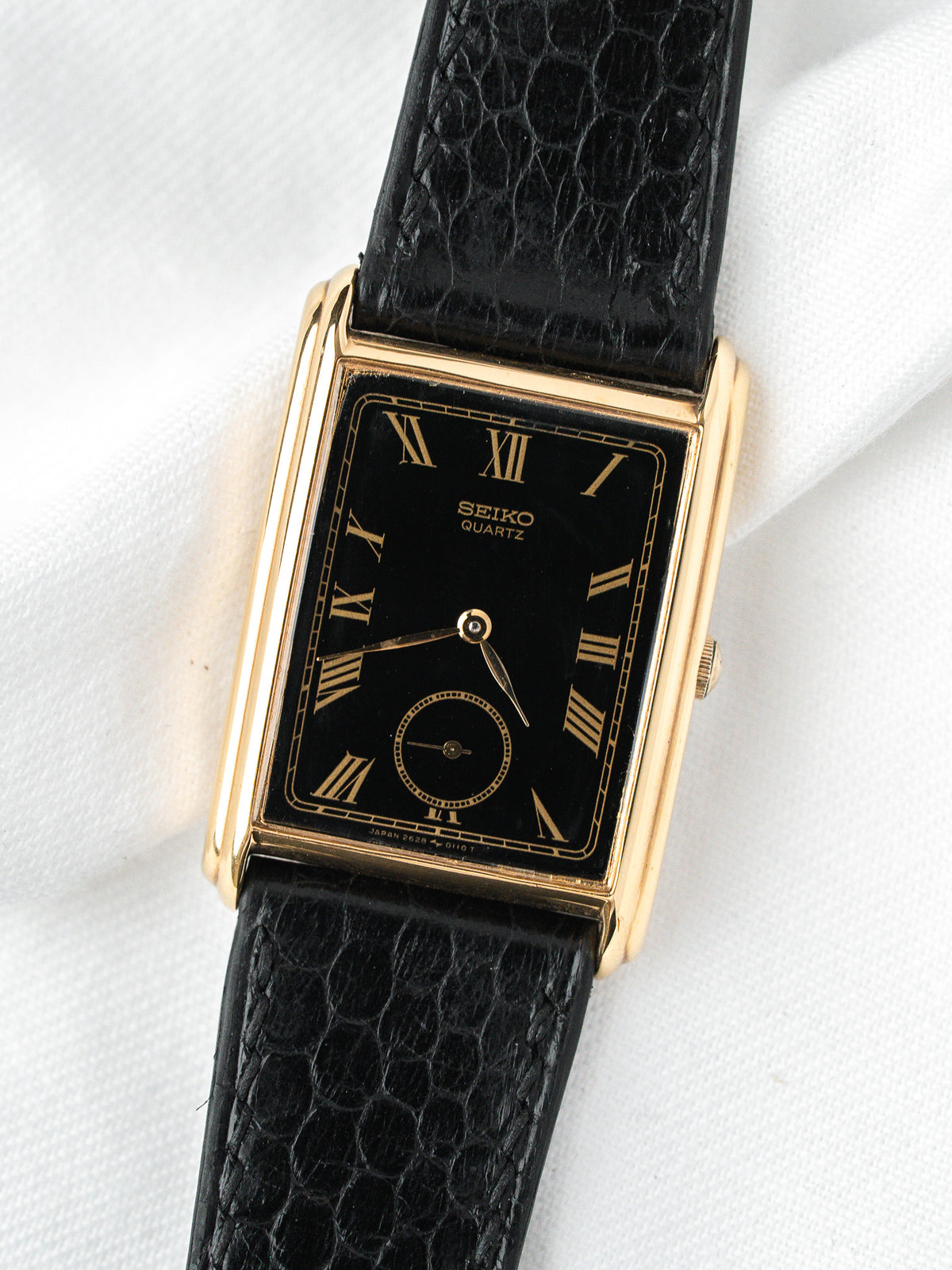 Seiko Quartz vintage watch with gold case, black dial, Roman numerals, and textured strap