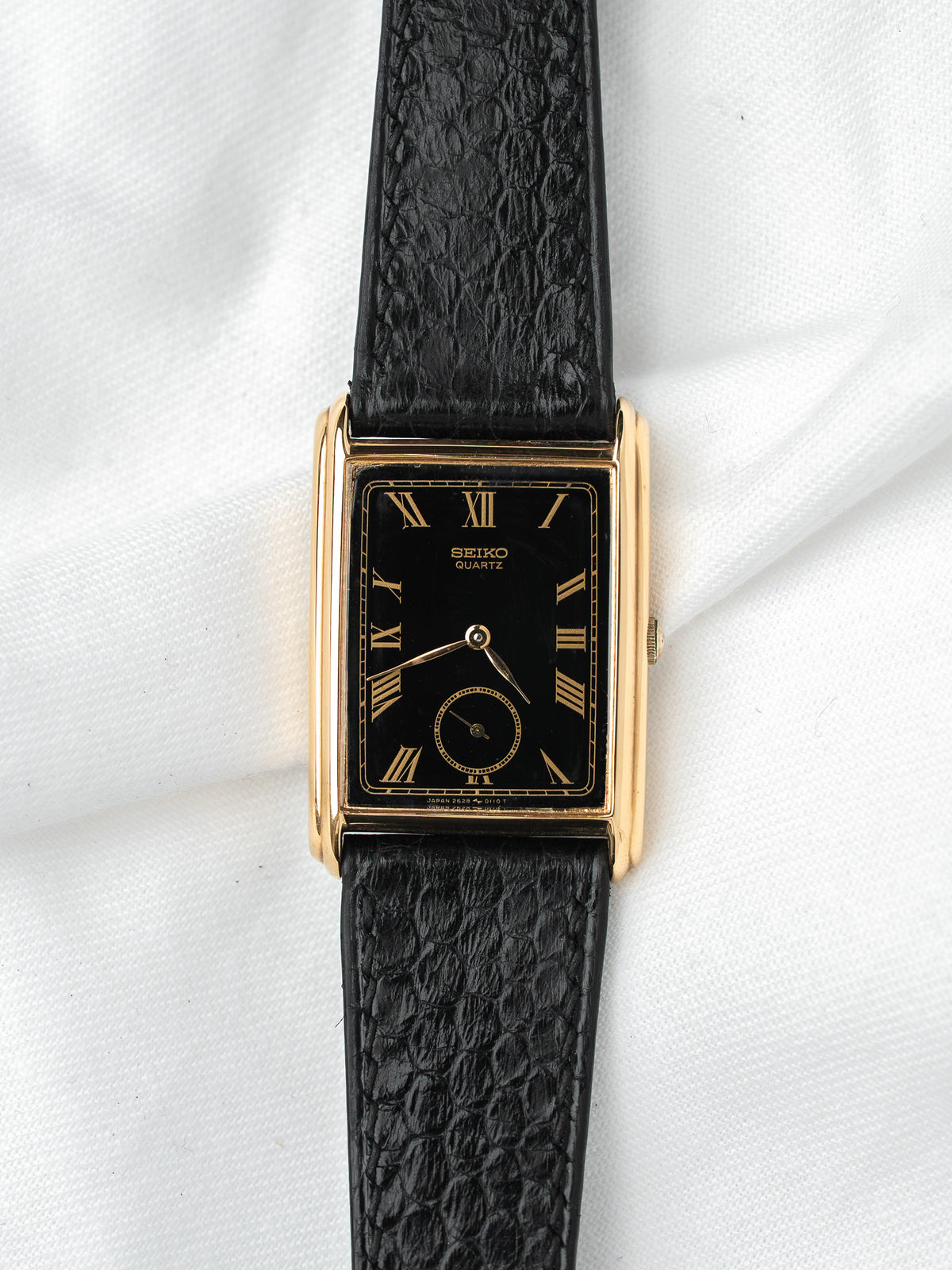 Seiko Quartz vintage watch with gold case, black dial, Roman numerals, and textured strap
