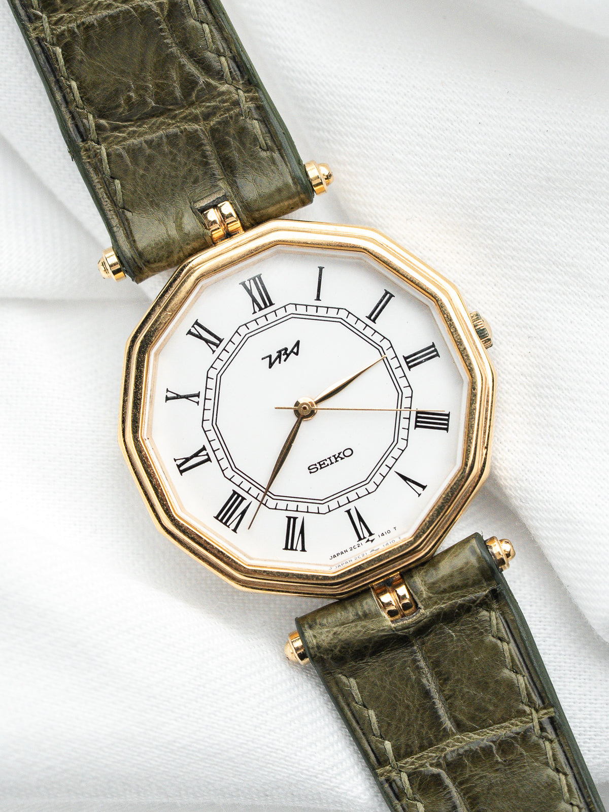 Montre Seiko vintage au boîtier octogonal doré et bracelet en cuir vert olive.