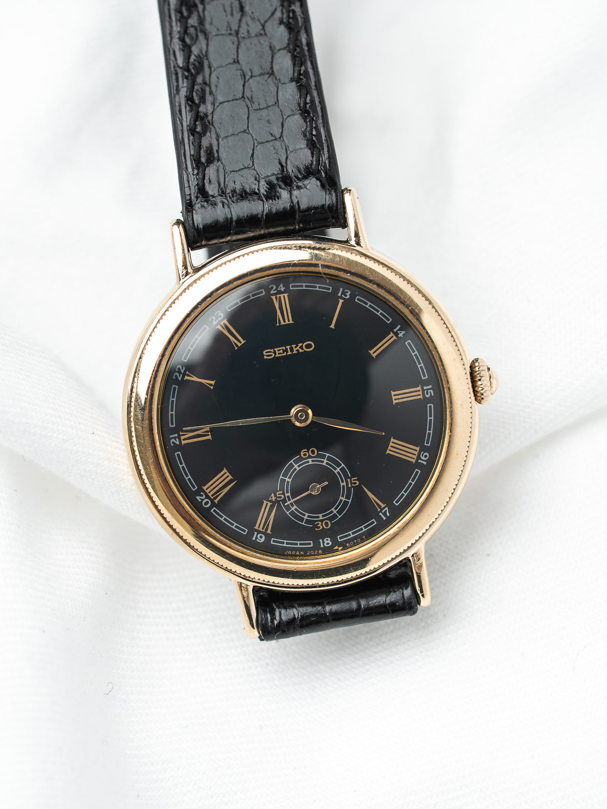 Seiko vintage watch with gold case, black dial, Roman numerals, and crocodile strap