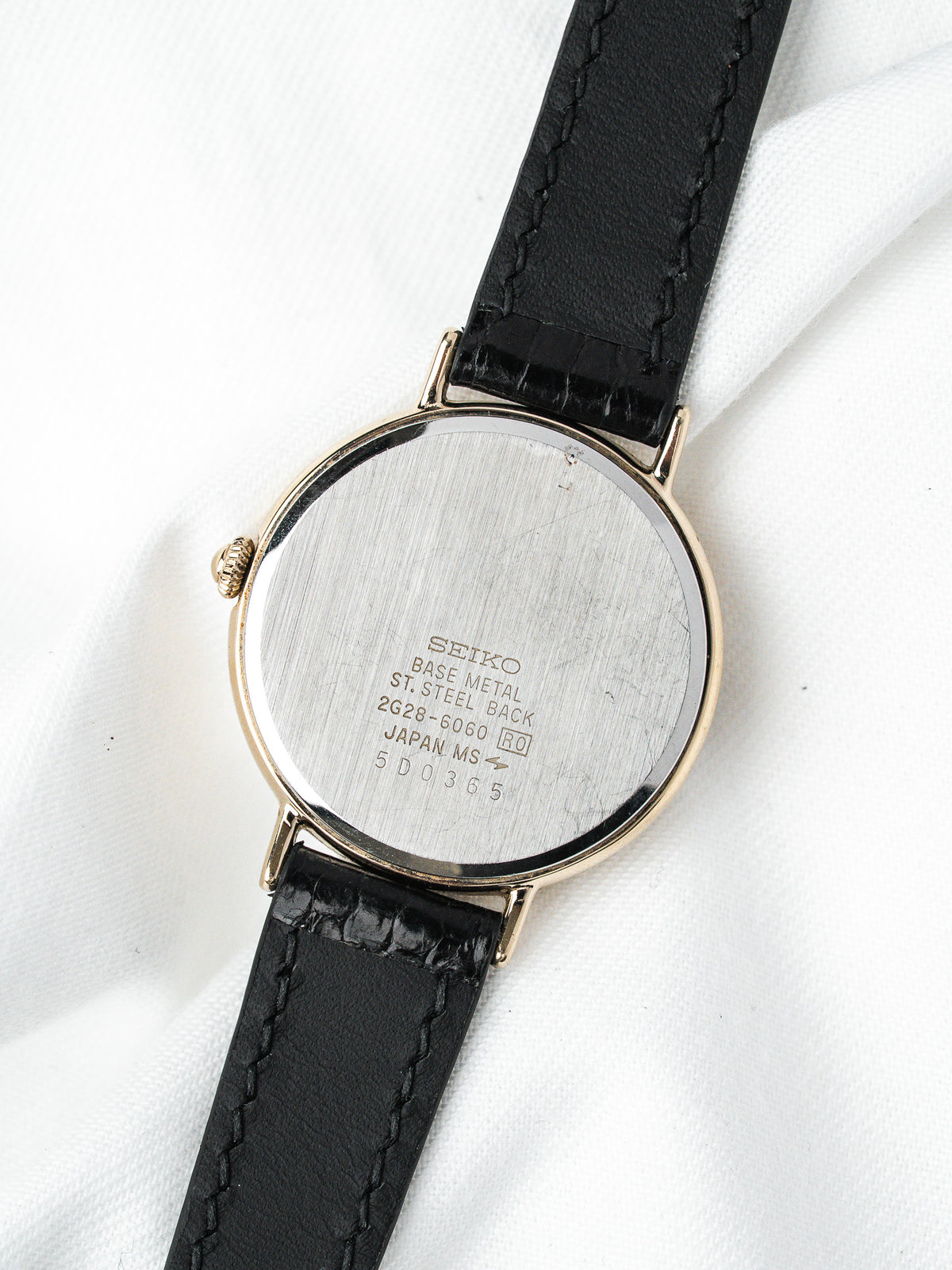Seiko vintage watch with gold case, black leather strap, steel back on white fabric