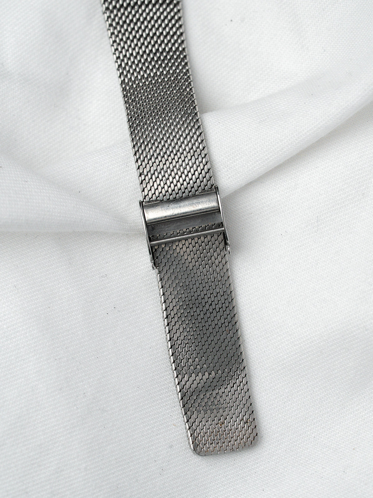 Vintage mesh watch strap in stainless steel, detailed clasp on white fabric