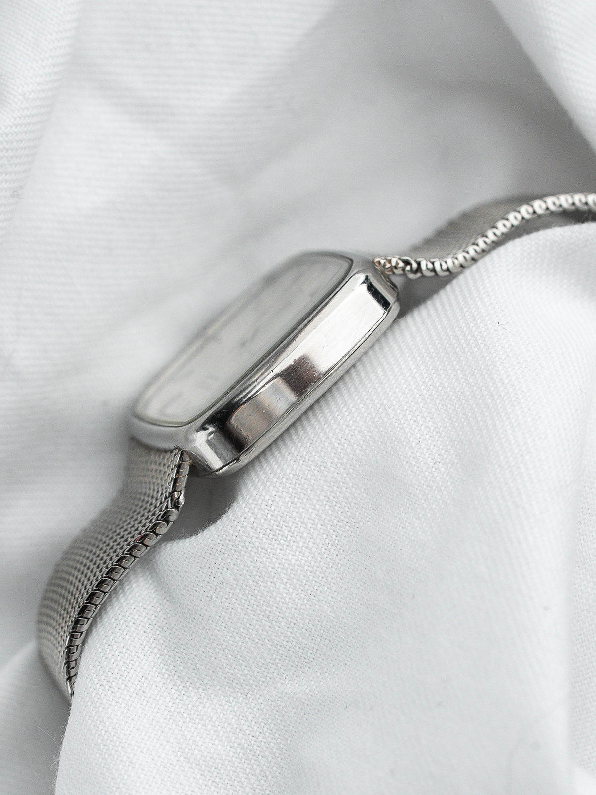 Montre vintage au boîtier rectangulaire en acier avec bracelet maille milanaise sur fond blanc