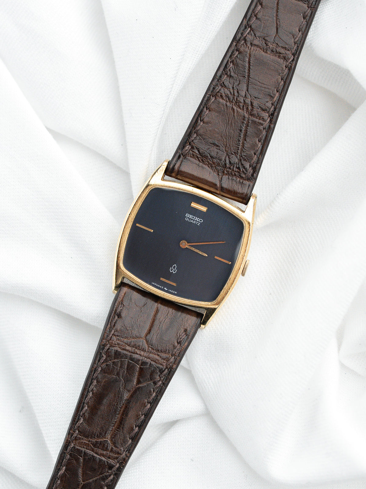 Montre Seiko Quartz vintage au cadran noir et bracelet en cuir marron texturé.