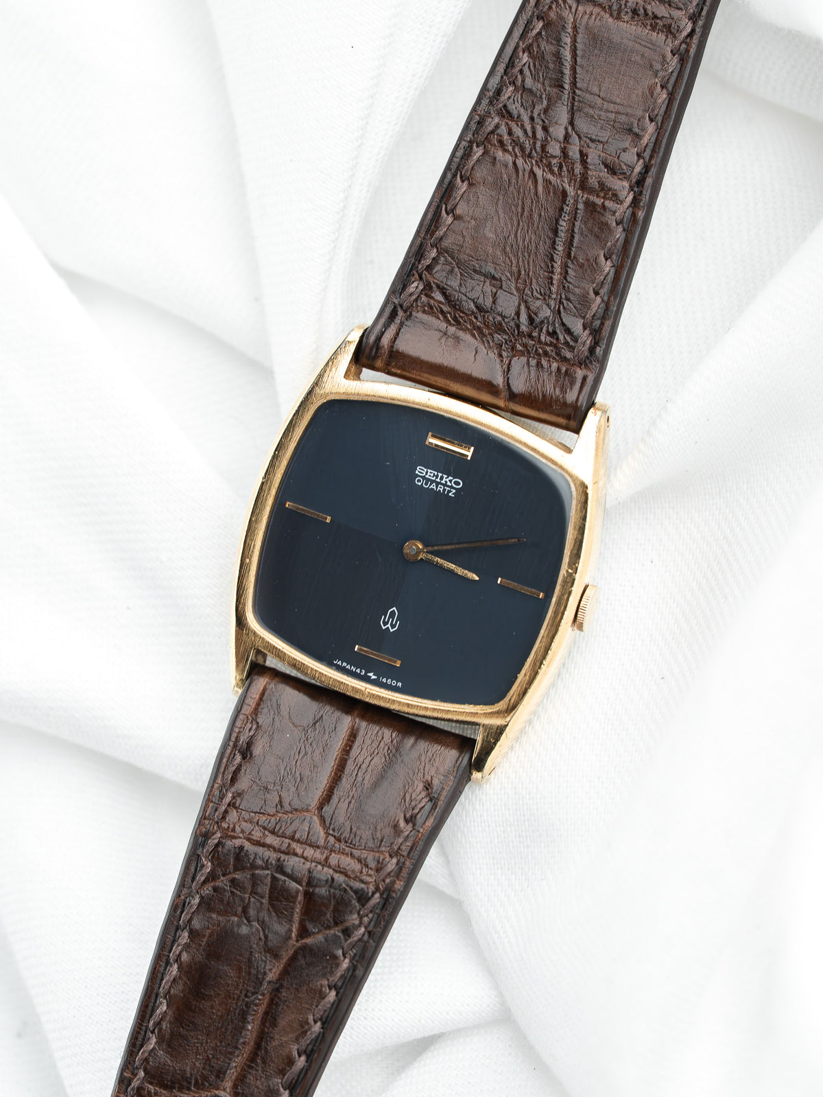 Montre Seiko Quartz vintage au boîtier doré rectangulaire et bracelet en cuir marron.