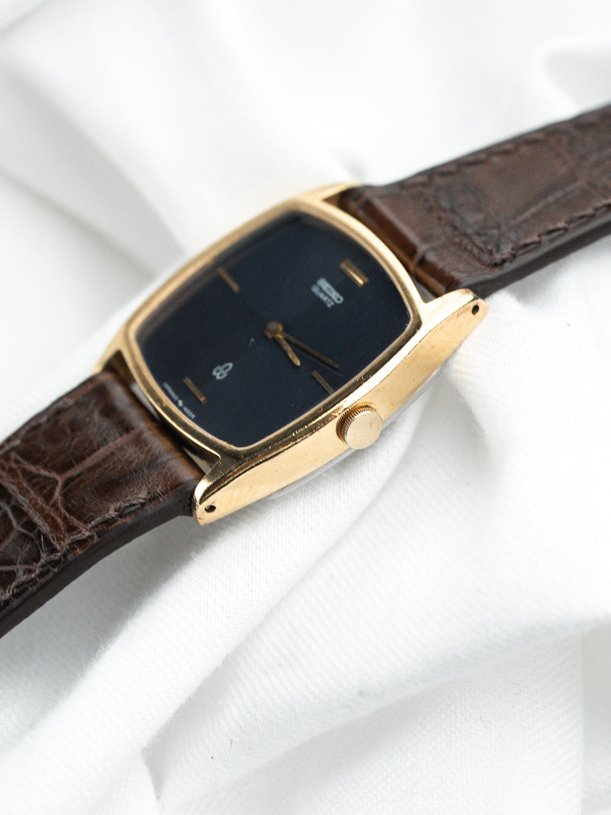 Montre vintage au boîtier rectangulaire doré, cadran bleu foncé et bracelet en cuir marron.