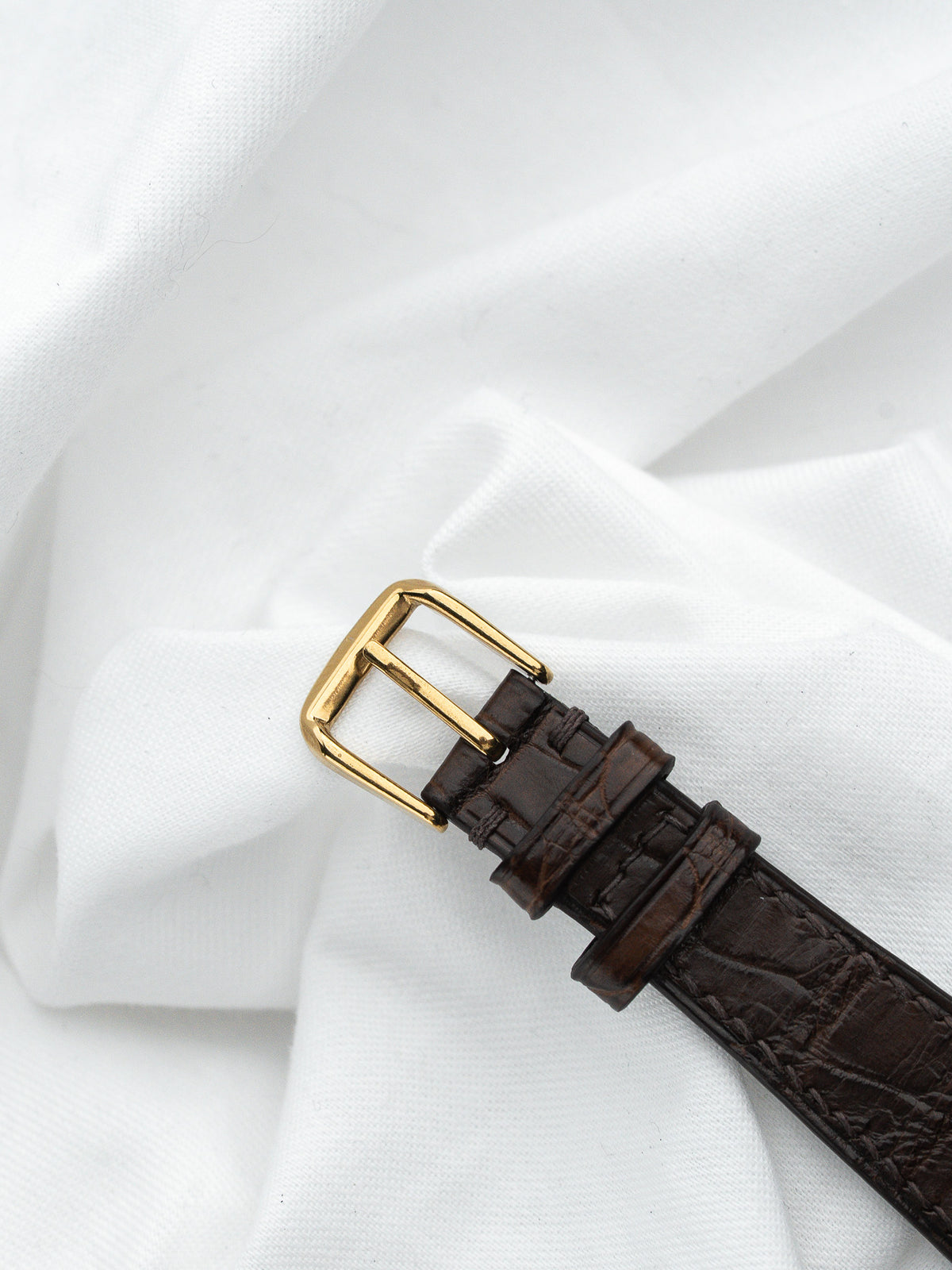 Boucle dorée d'un bracelet de montre en cuir marron texturé sur fond blanc.