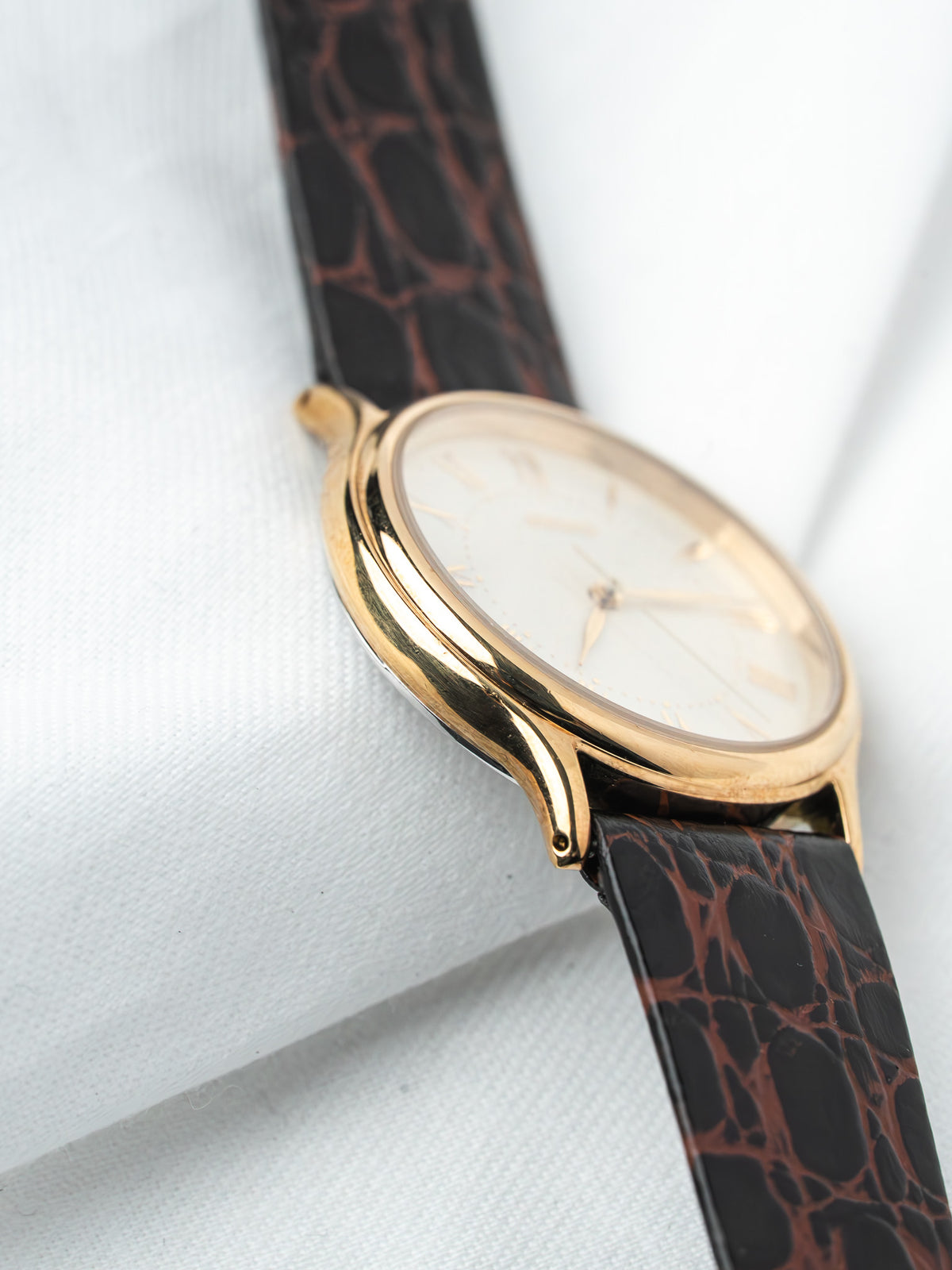 Vintage watch with gold case, white dial, and brown crocodile strap on white background