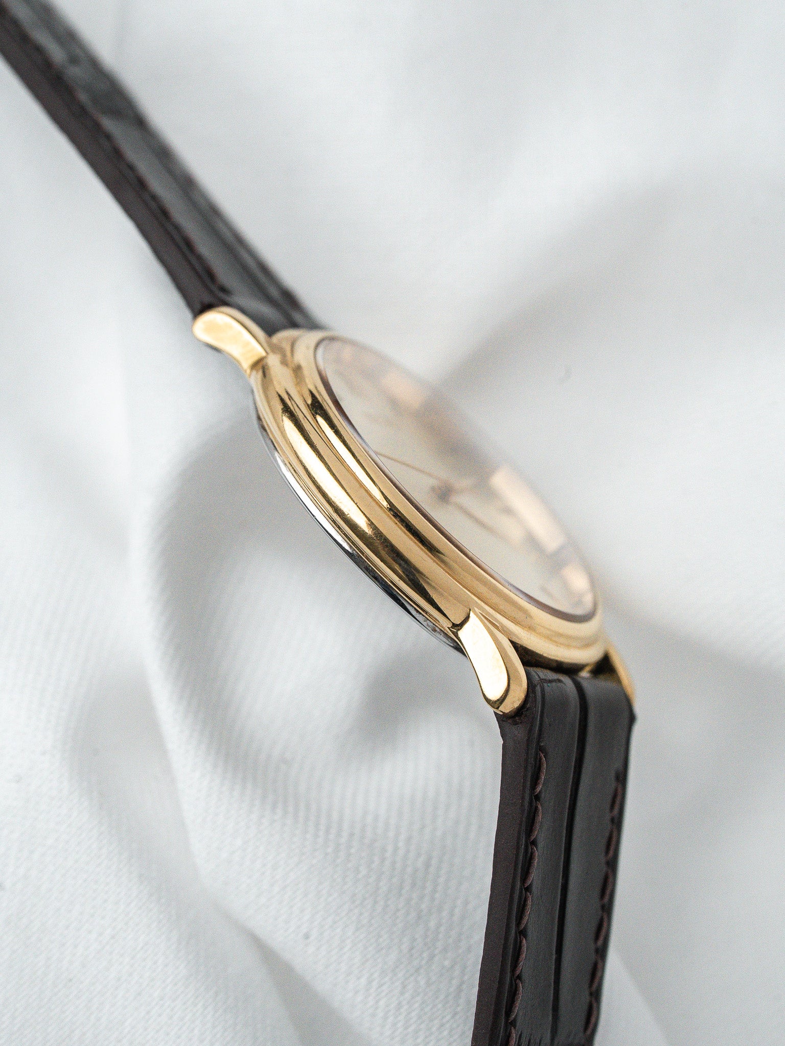 Vintage Cartier watch with gold case and black leather strap on white fabric