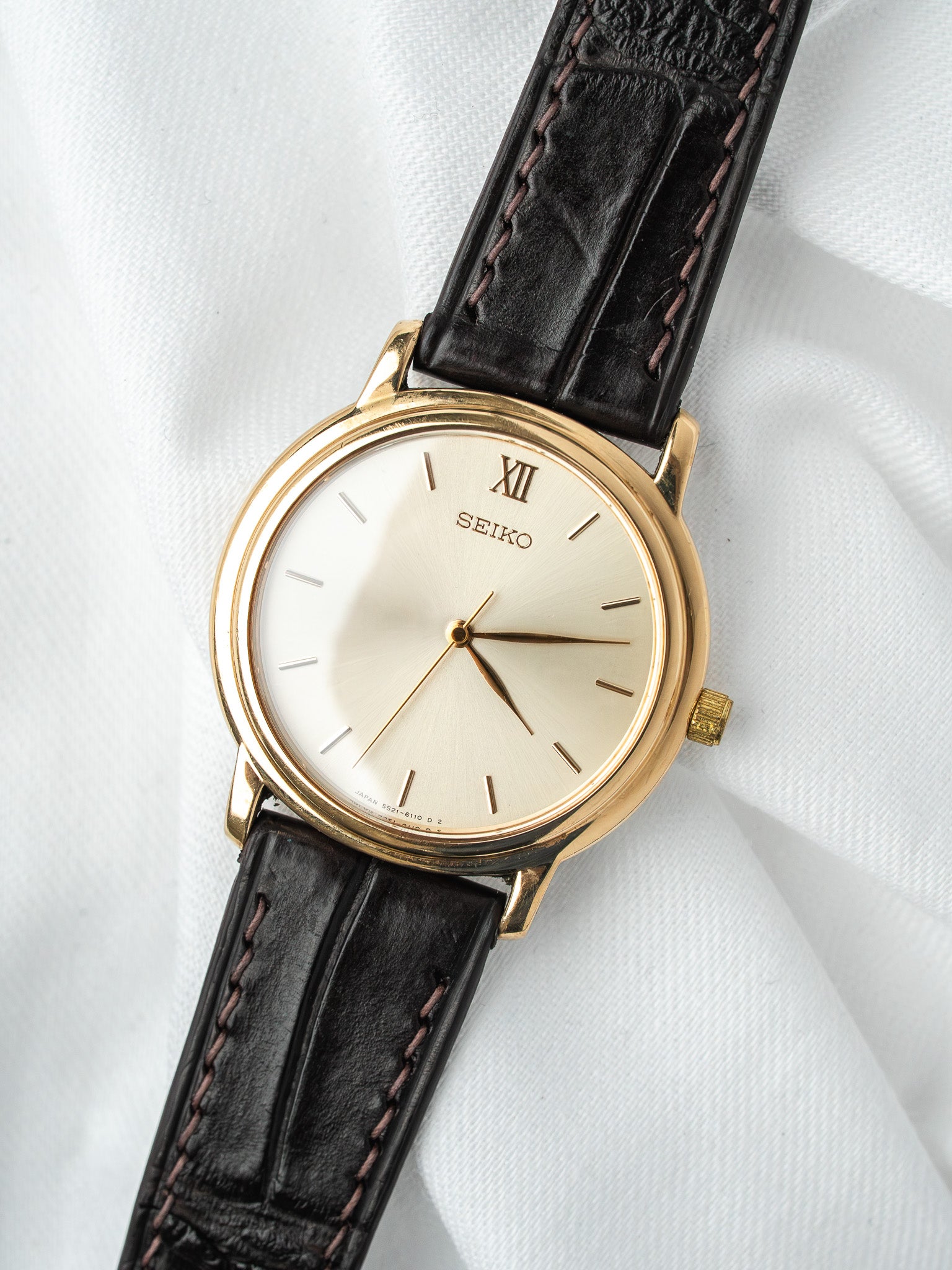 Seiko vintage watch with gold case, cream dial, black leather strap on white fabric