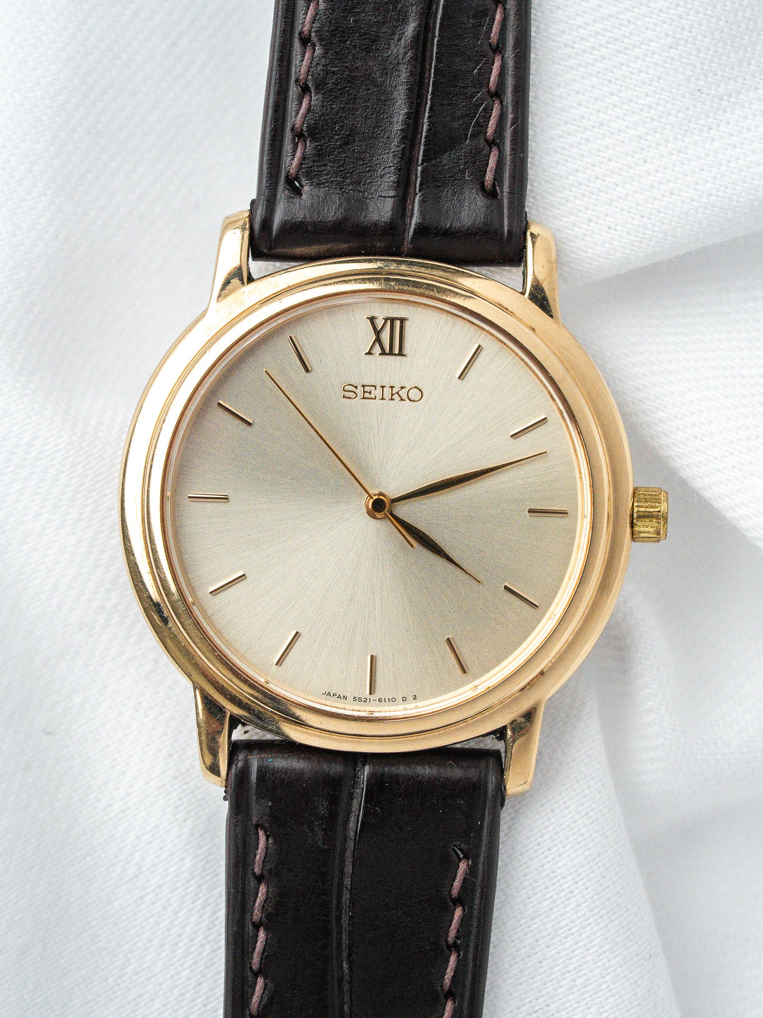 Seiko vintage watch with gold case, silver dial, Roman XII, black leather strap