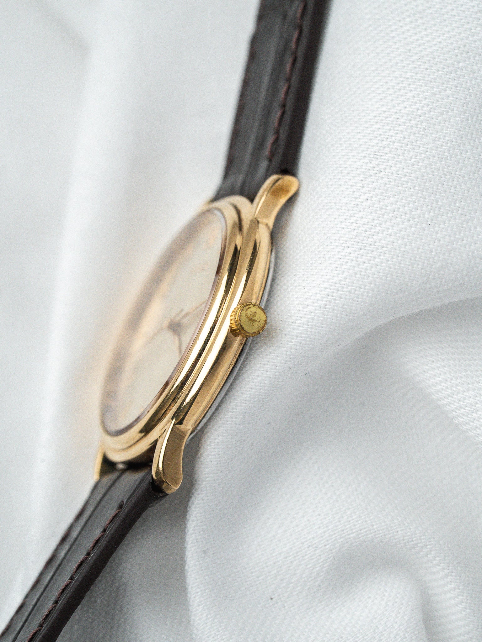 Vintage gold watch with black leather strap on white fabric background