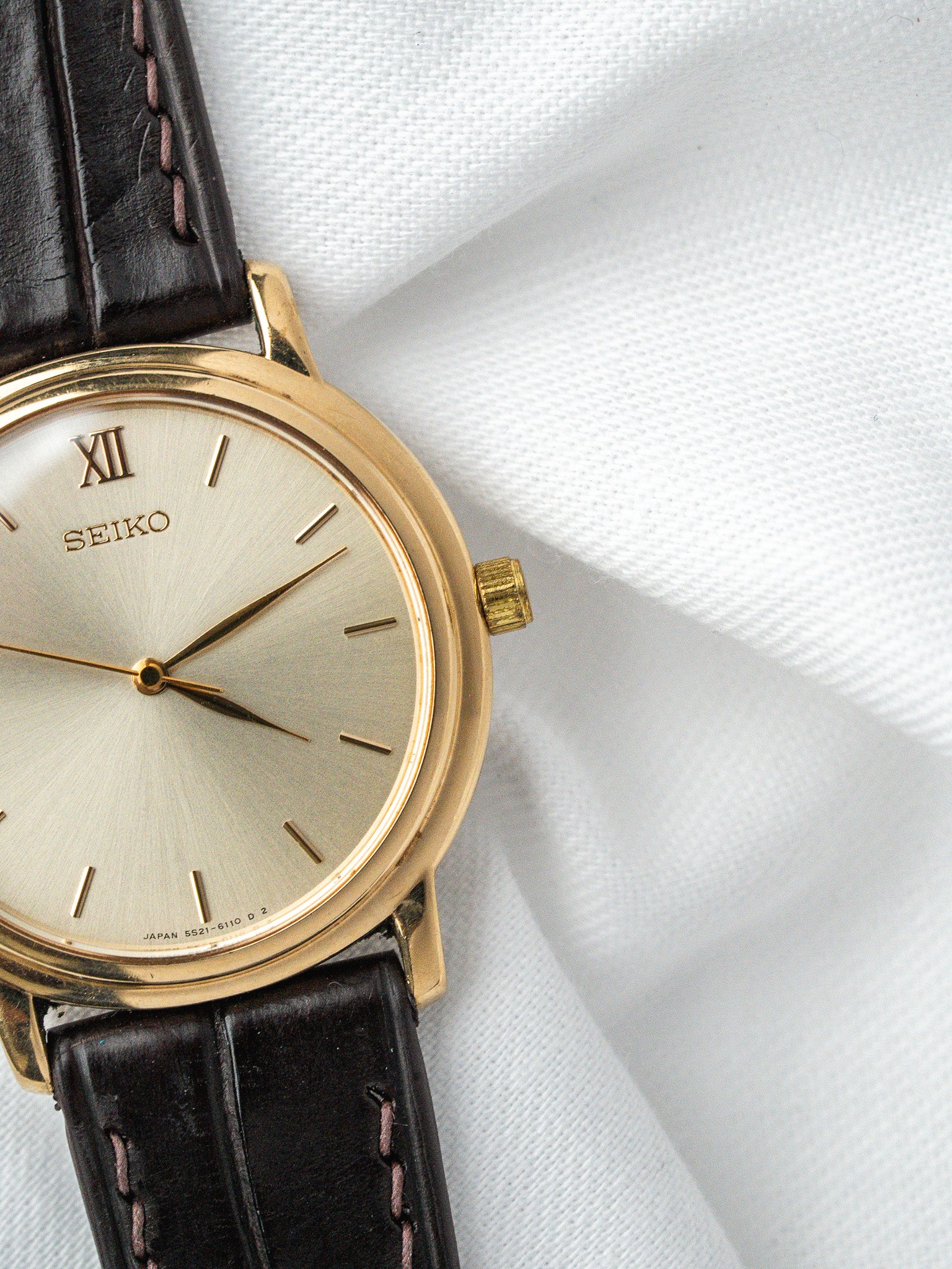 Vintage Seiko watch with gold case, silver dial, Roman numeral XII, black leather strap
