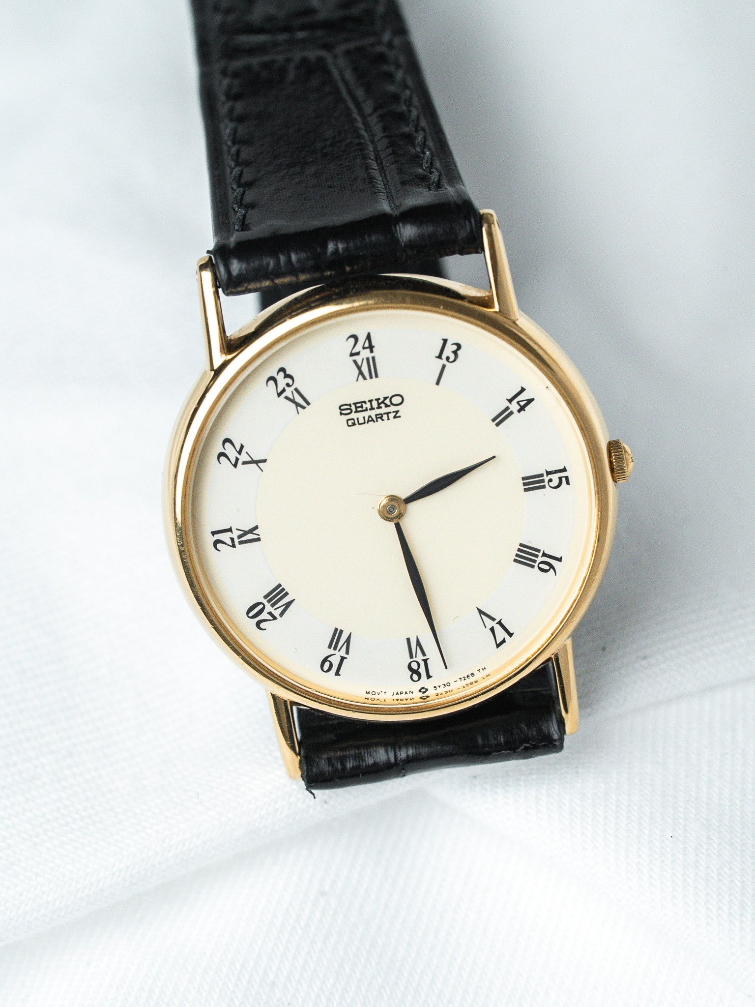 Seiko Quartz vintage watch with gold case, cream dial, black leather strap on white background