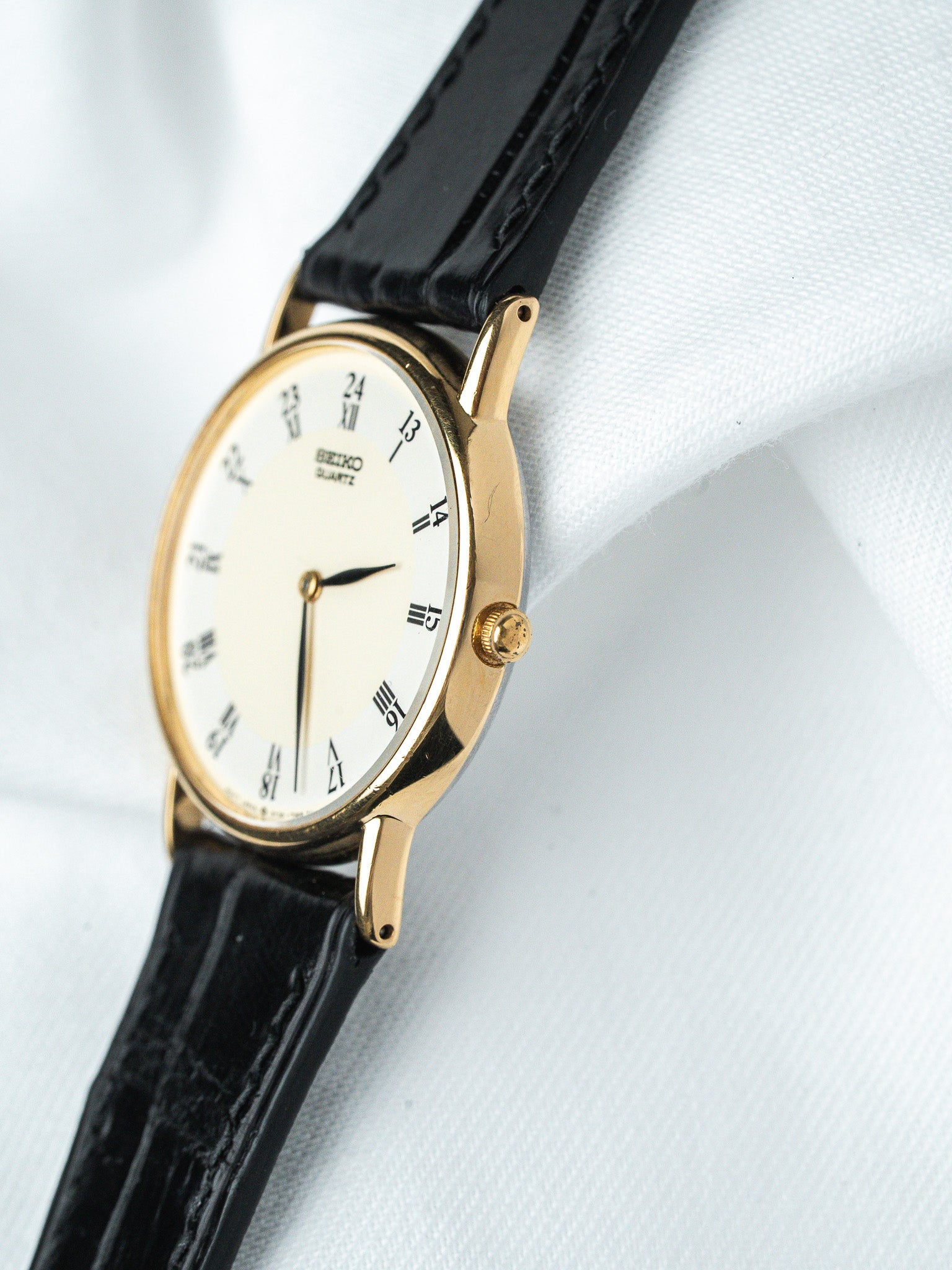 Seiko vintage watch with gold case, white dial, black leather strap on white fabric