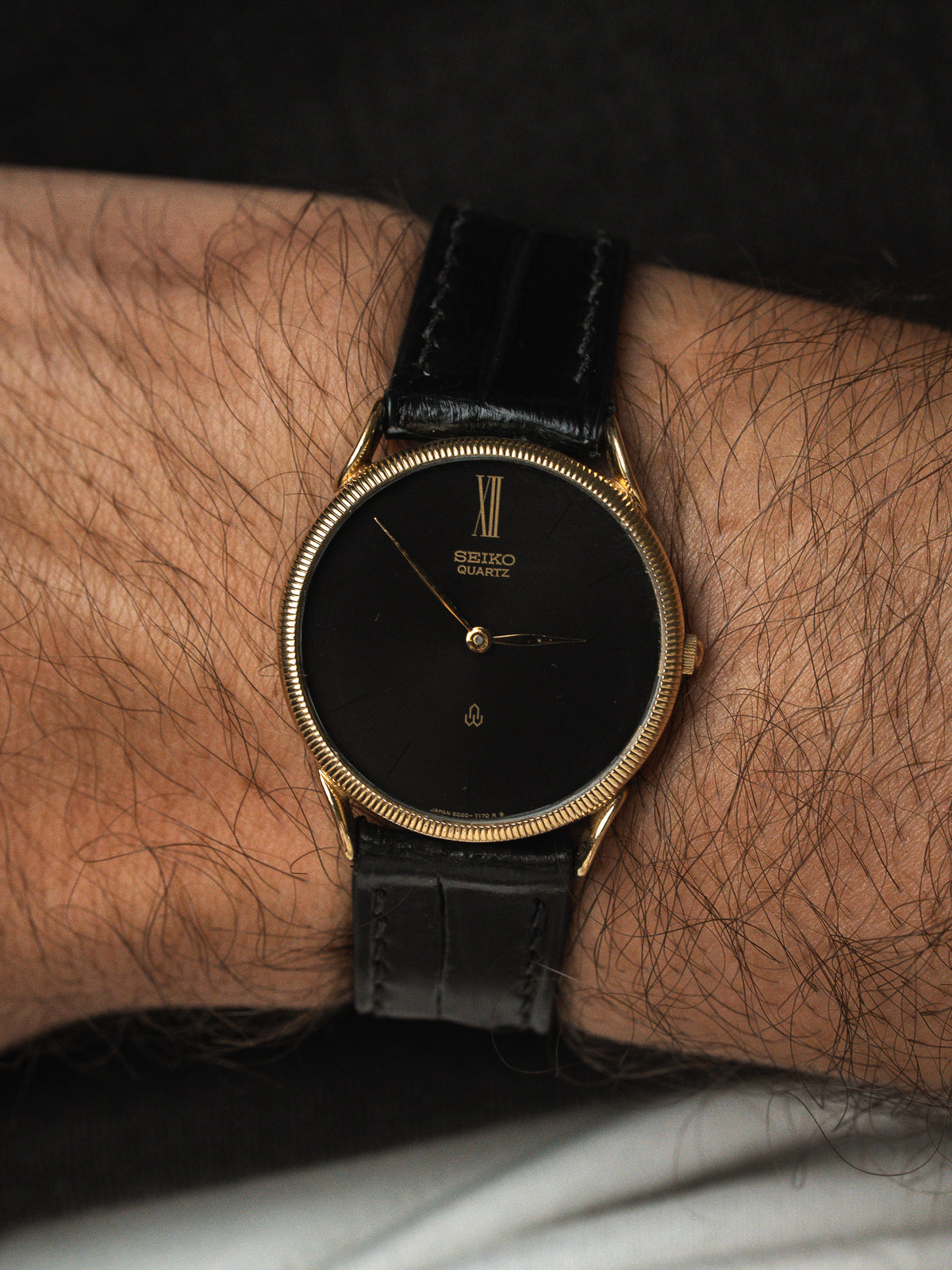 Montre Seiko Quartz vintage, cadran noir et boîtier doré, bracelet cuir noir au poignet